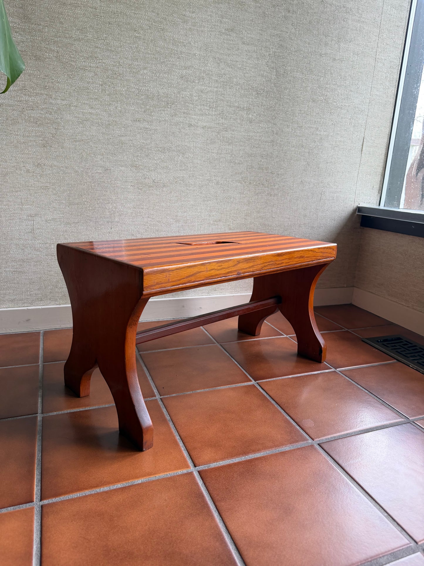 Wooden stool on a tiled floor with a textured wall in the background