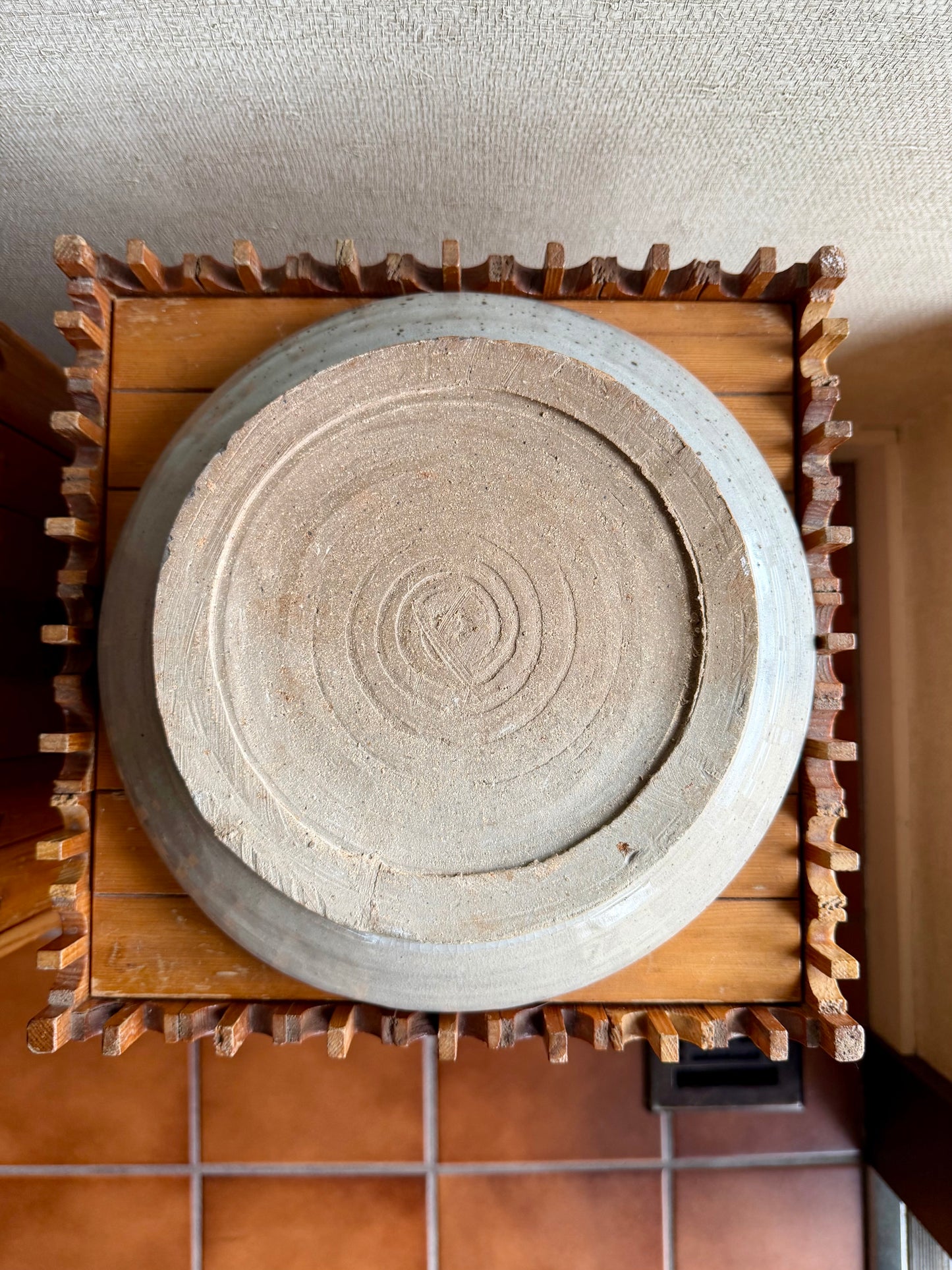 Ceramic plate with concentric circle design on a wooden stand against a textured wall.