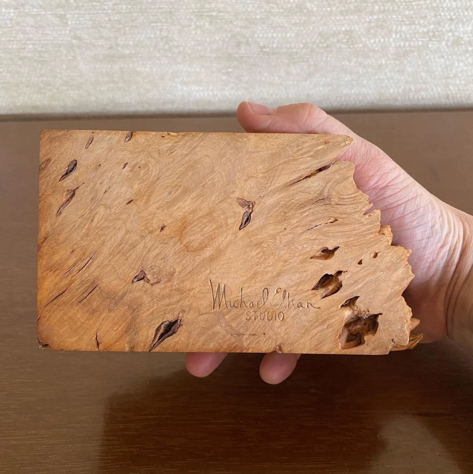 Hand holding a piece of wood with 'Michael Orian Studio' engraved on it.