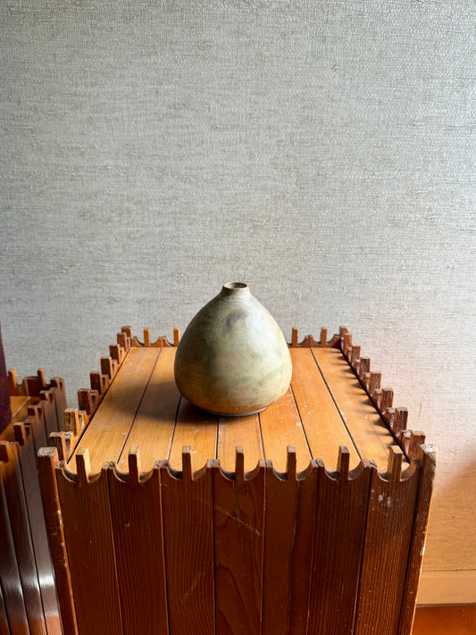 Decorative vase on a wooden stand against a textured wall.