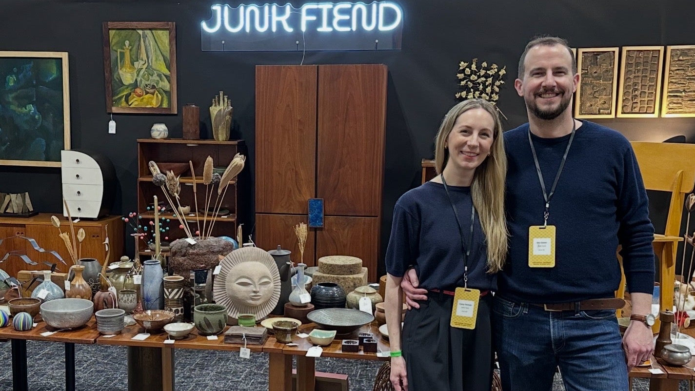 Two people standing in front of a table with various items at an event called 'Junk Fiend'.