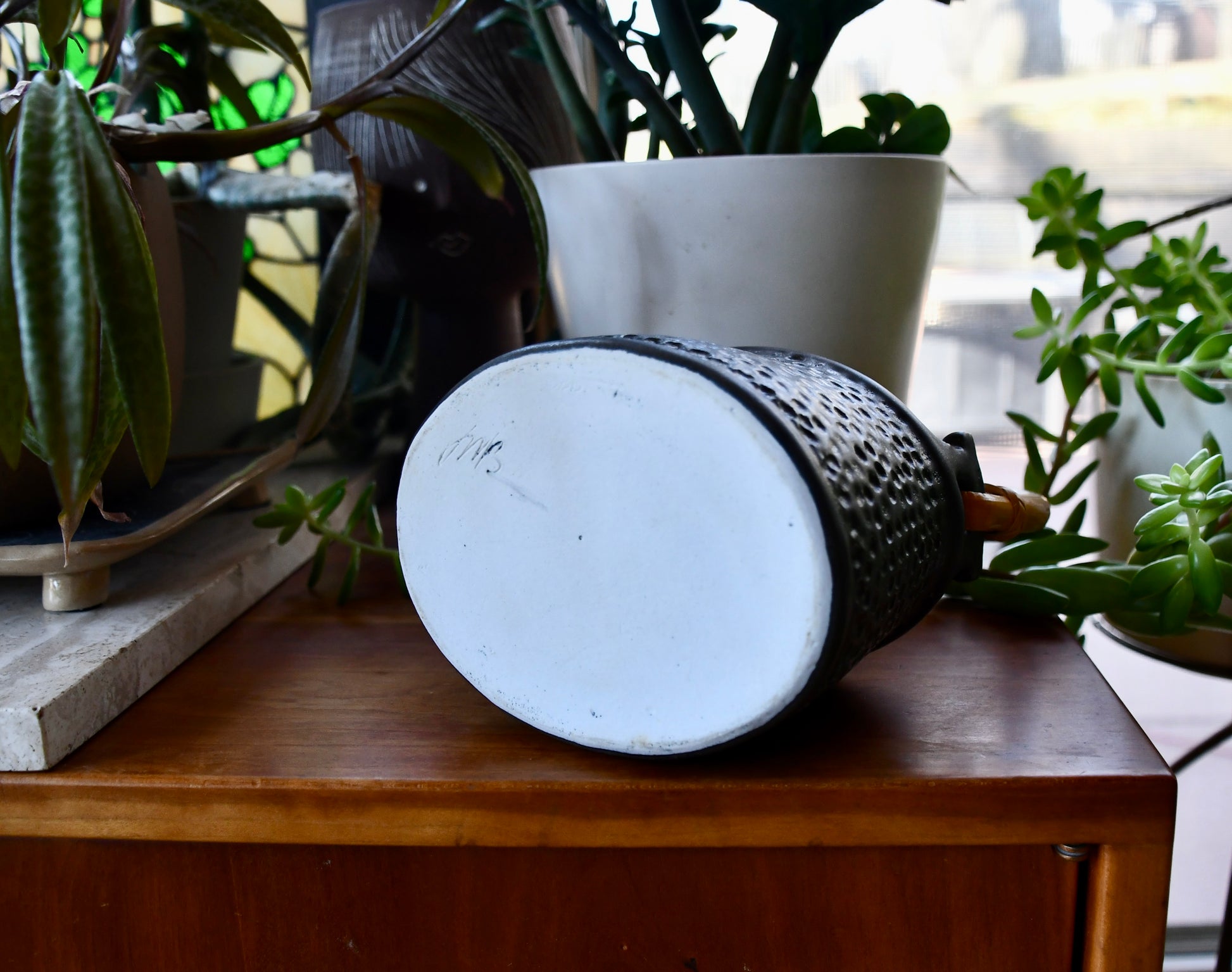 Cylindrical ceramic pot on a wooden surface with plants in the background