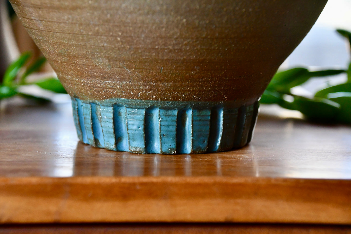 Ceramic pot with textured brown body and blue rim on a wooden surface