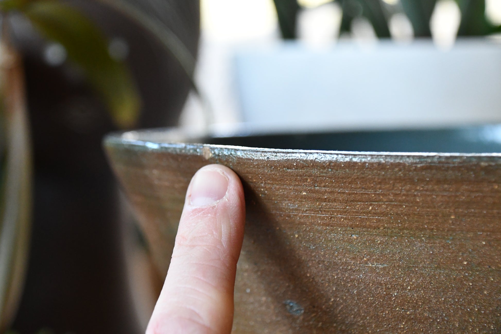 Close-up of a hand holding a textured ceramic bowl with a blurred background