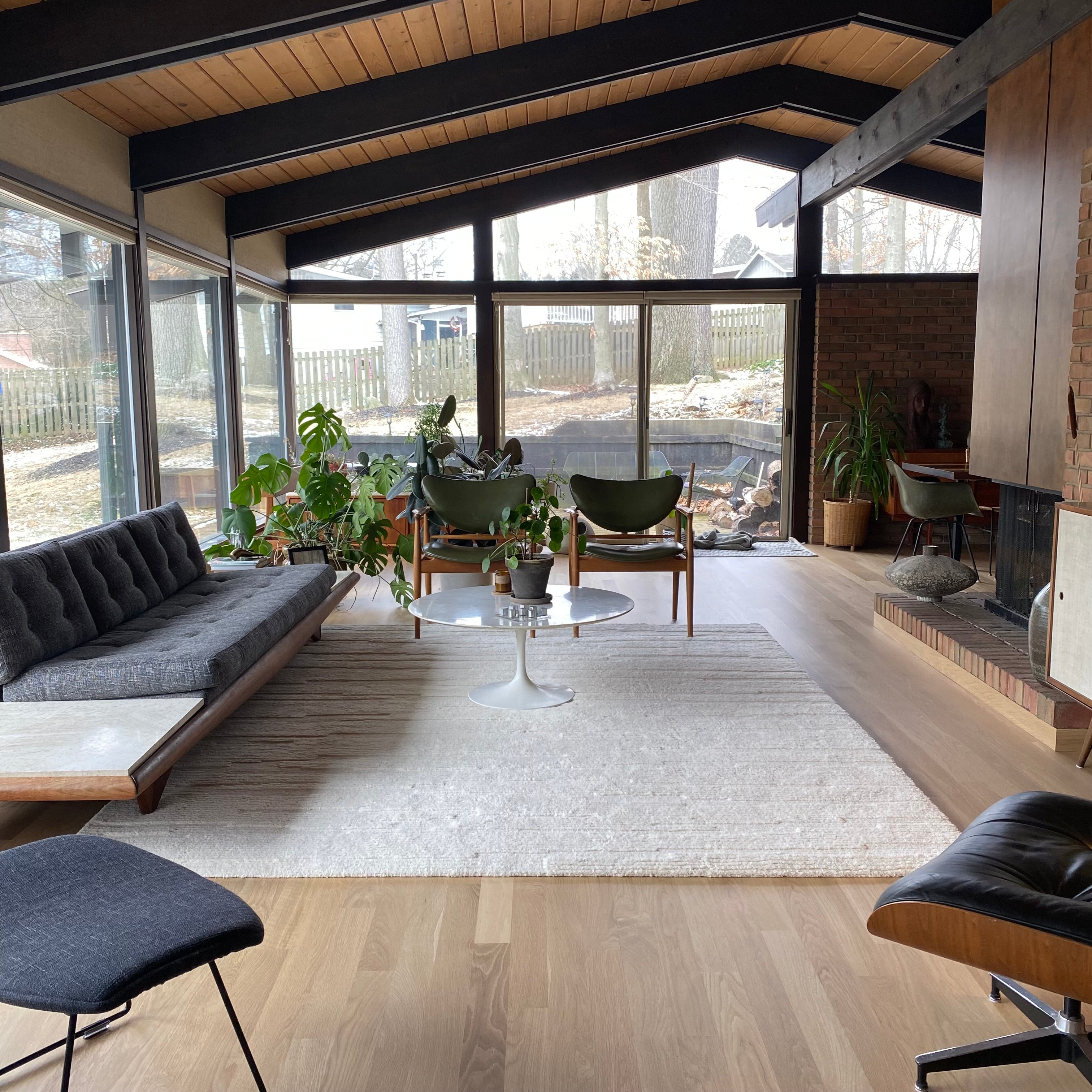 A photo of a mid-century modern living room with wood floors and big windows.