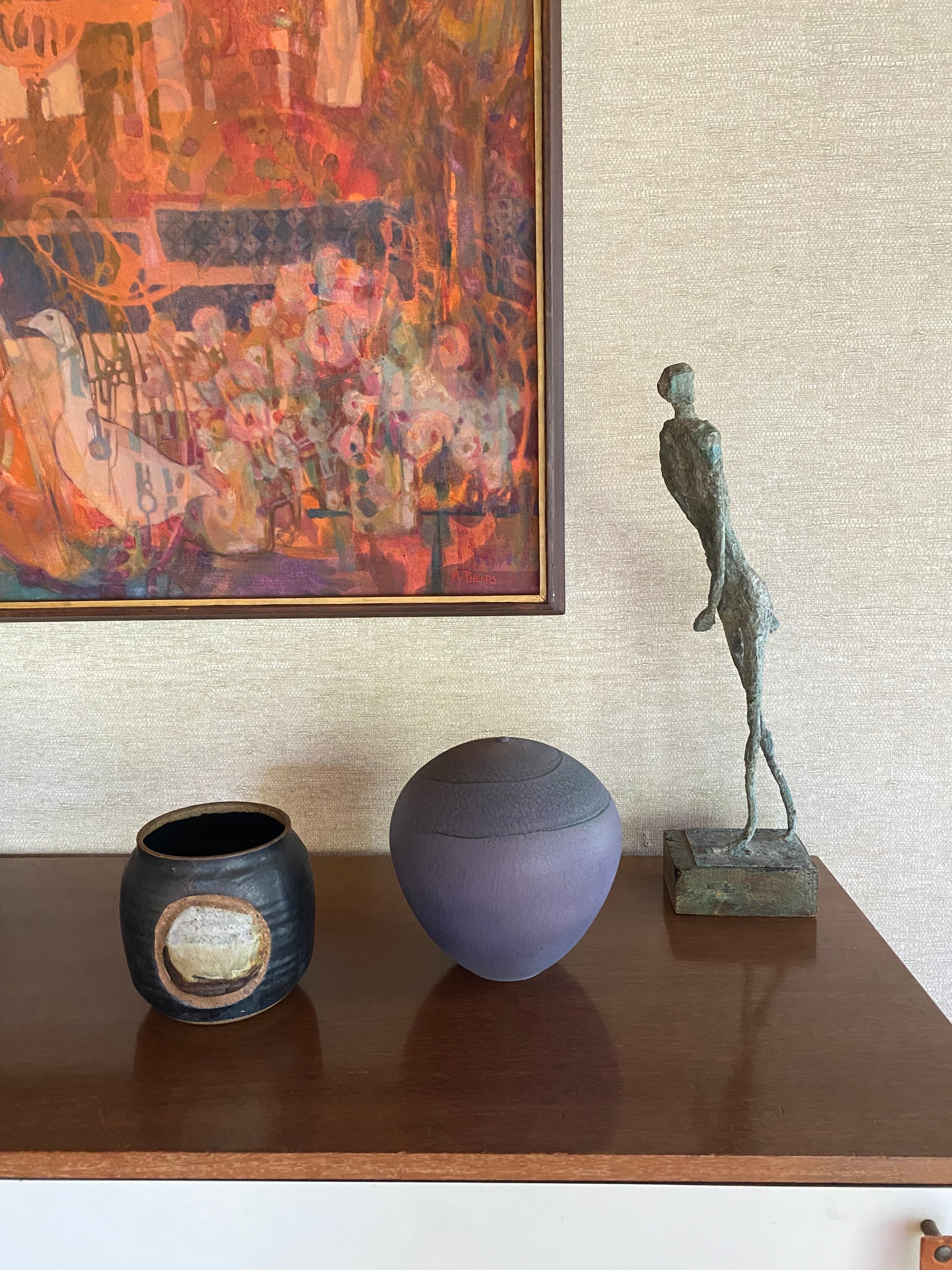 Abstract painting on the left, bronze sculpture above, and two ceramic vases below on a textured wall.