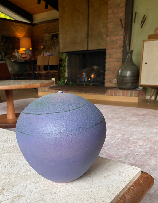 Purple ceramic sphere on a textured surface with a living room in the background