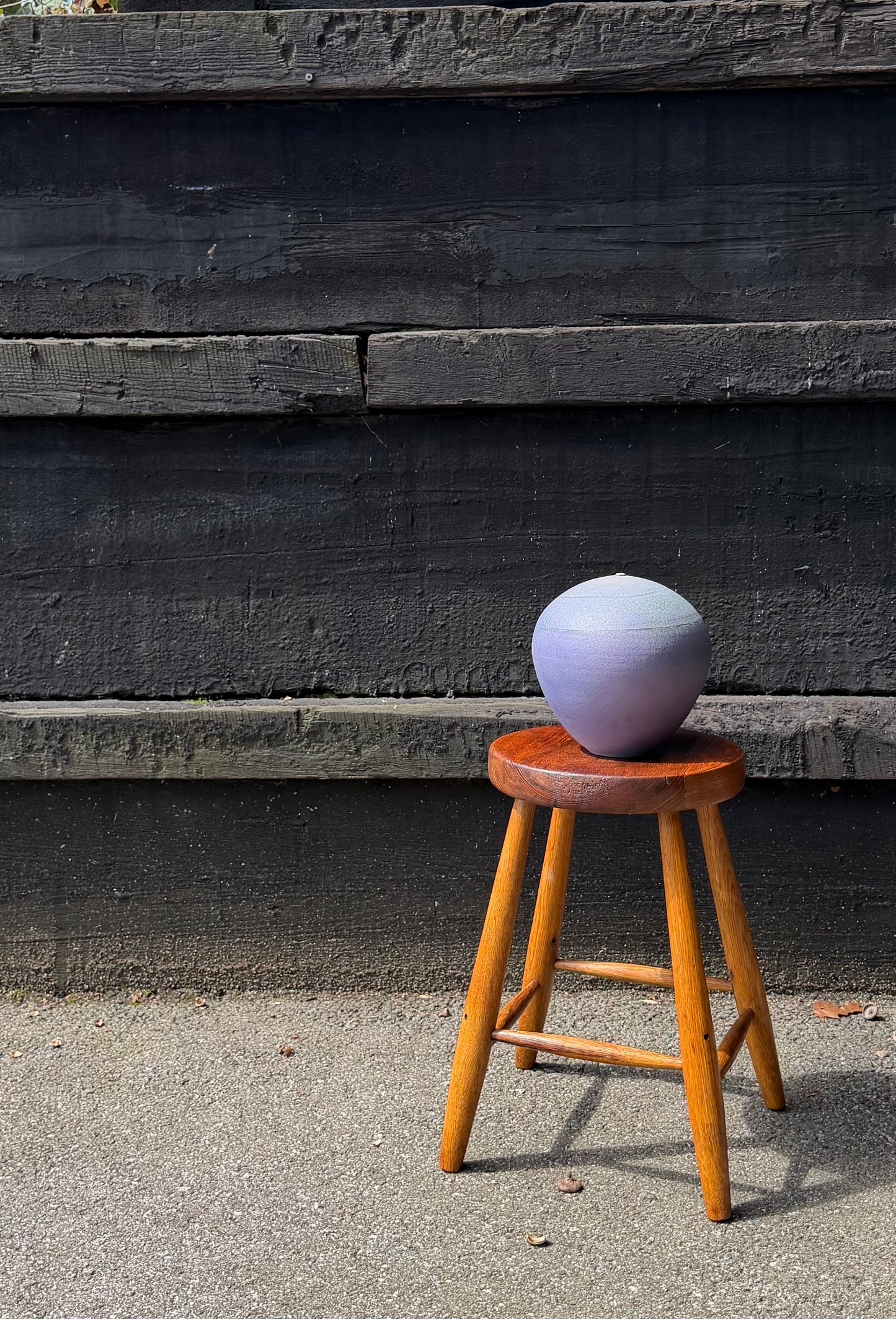 Purple ceramic sphere on a wooden stool against a dark wooden wall.