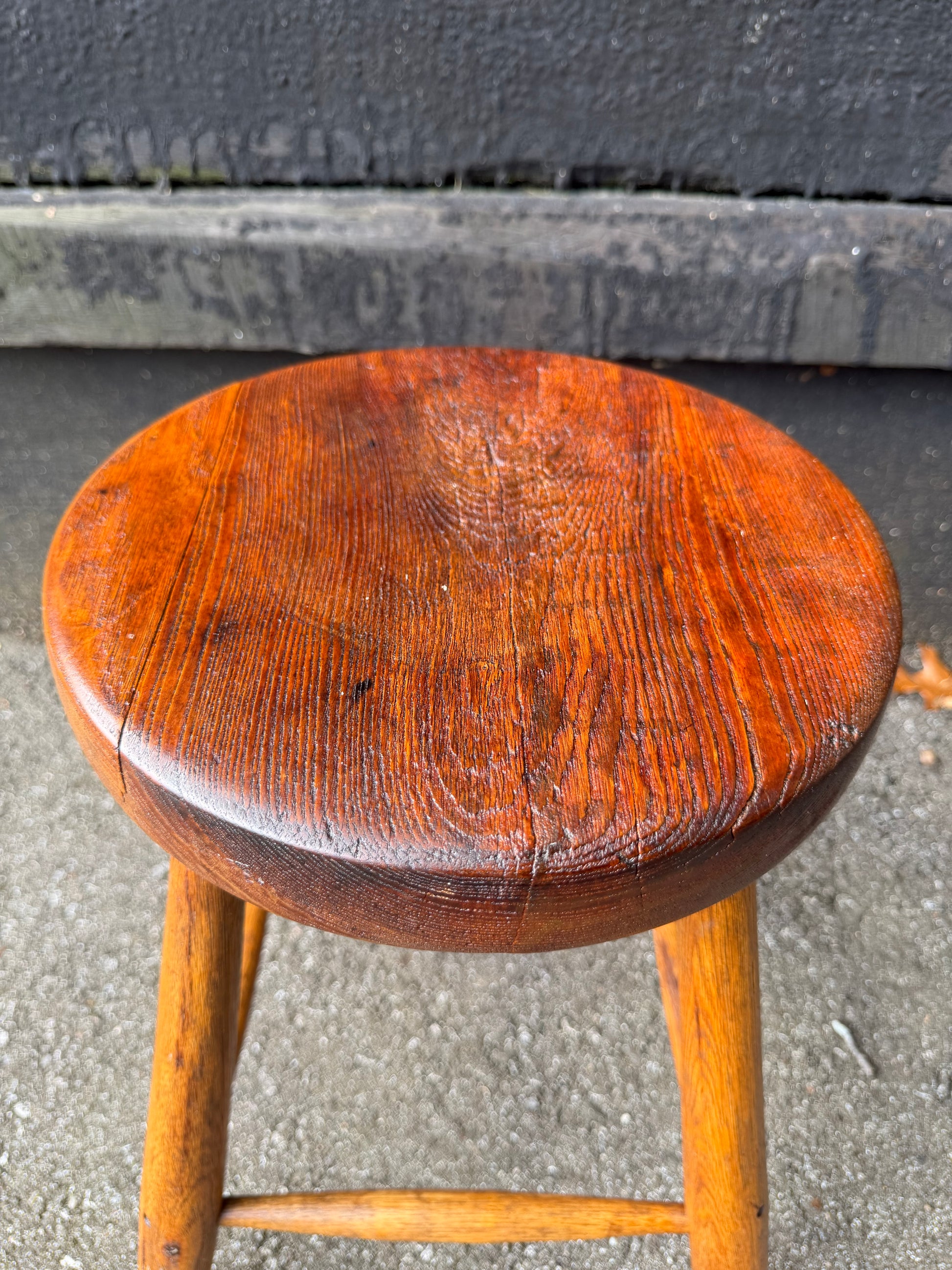 Wooden stool with a worn seat on a concrete surface