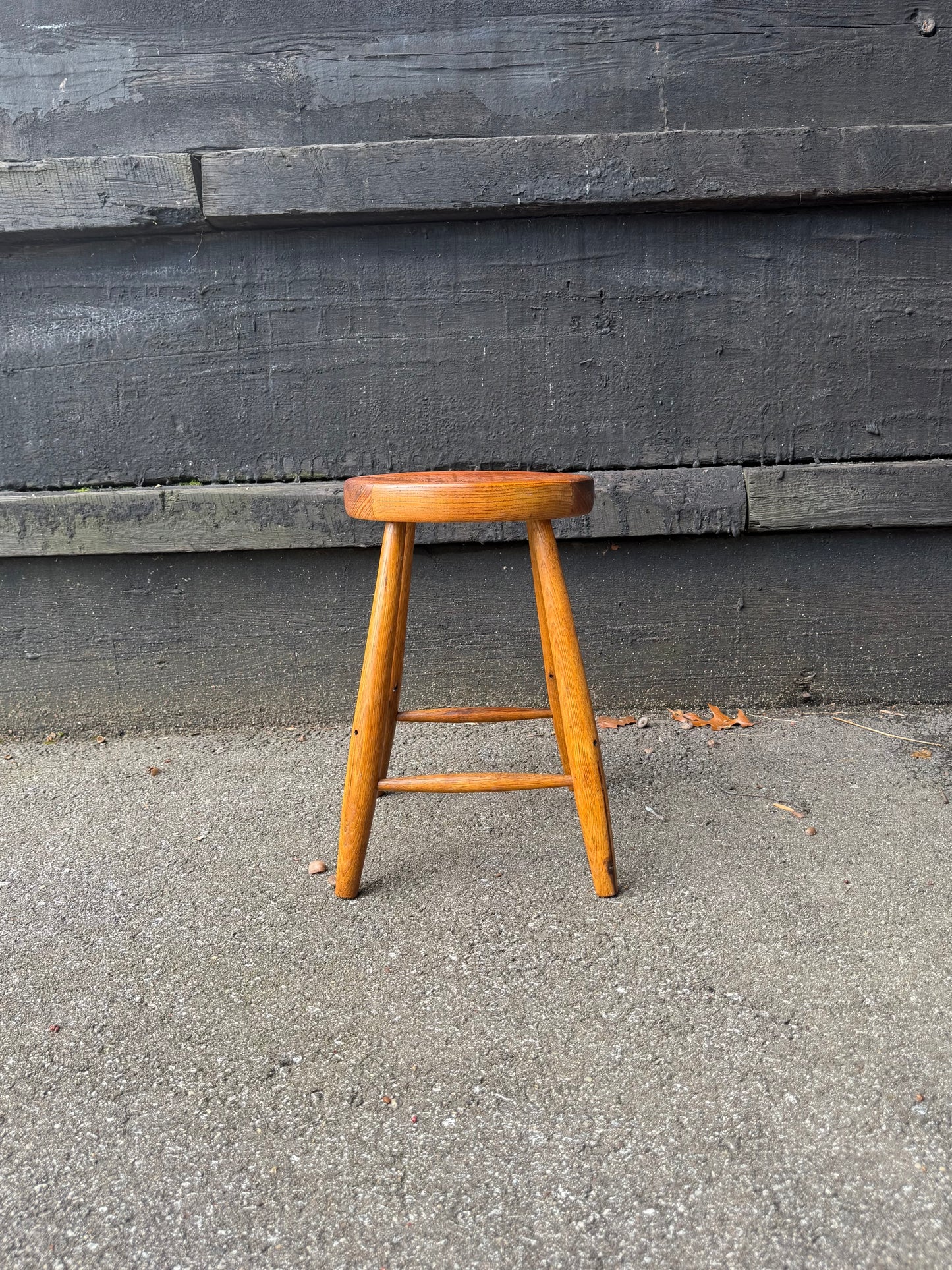 Wooden stool on a concrete surface with a dark wooden wall in the background