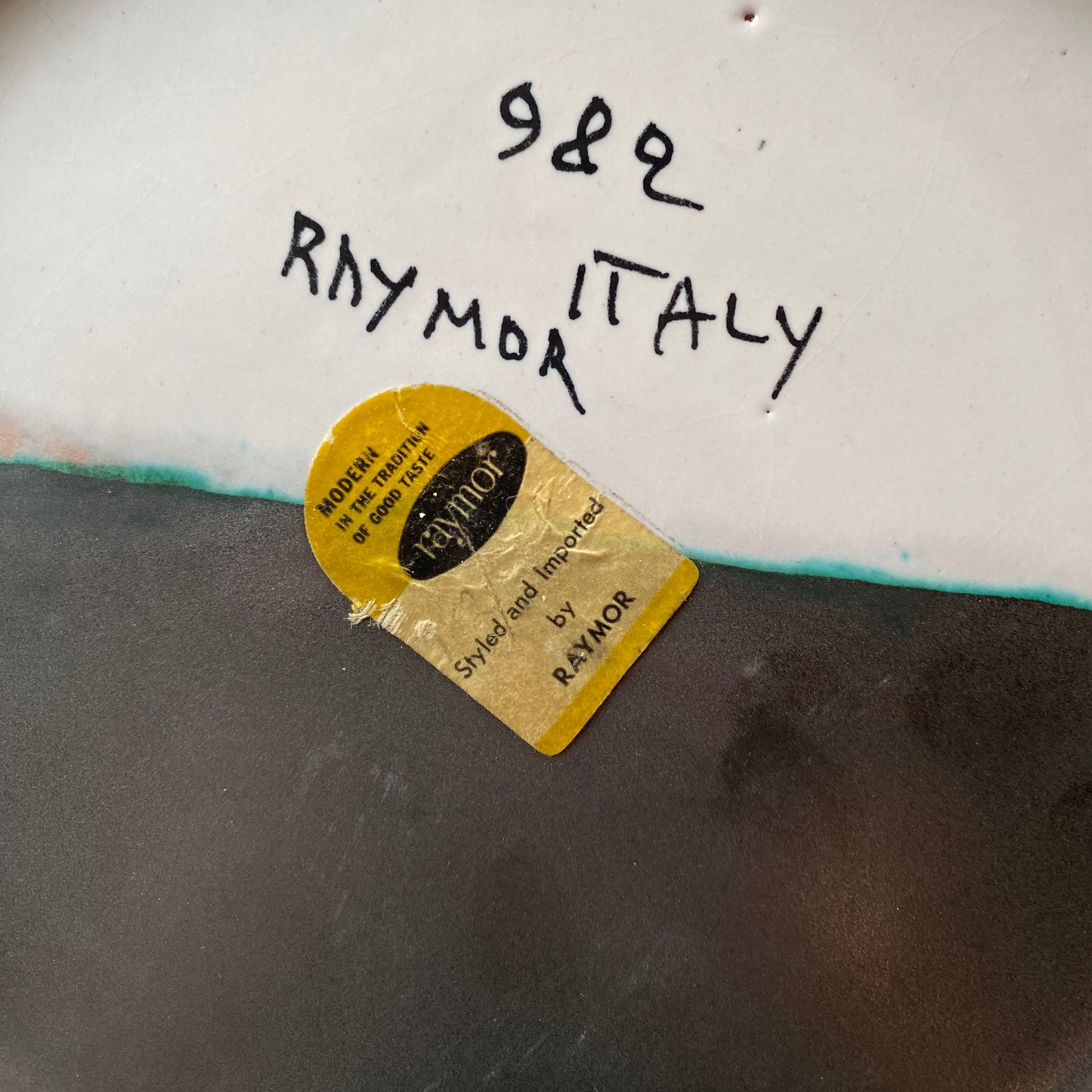 Close-up of a ceramic plate with 'Raymo Italy' branding and a gold label.