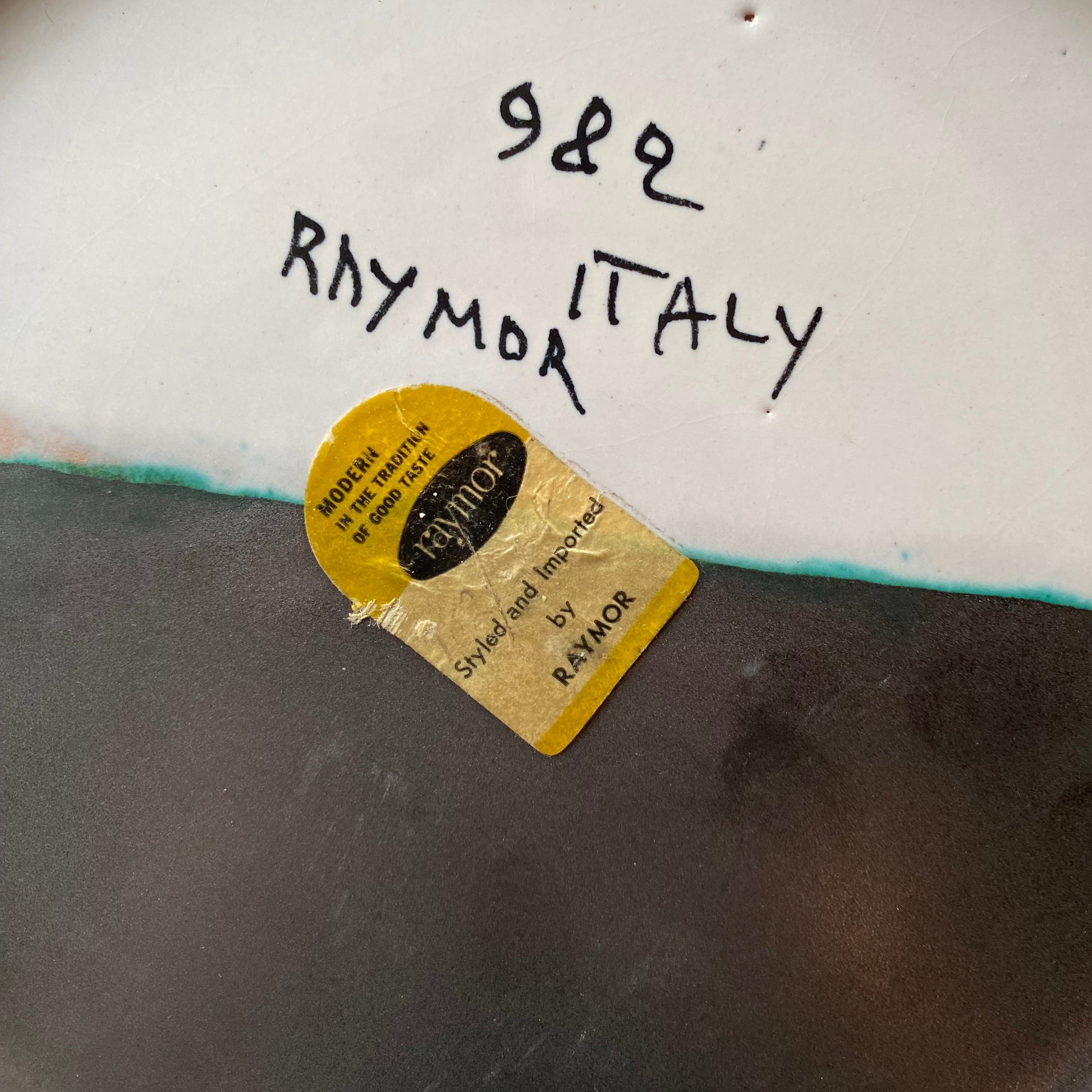 Close-up of a ceramic plate with 'Raymo Italy' branding and a gold label.