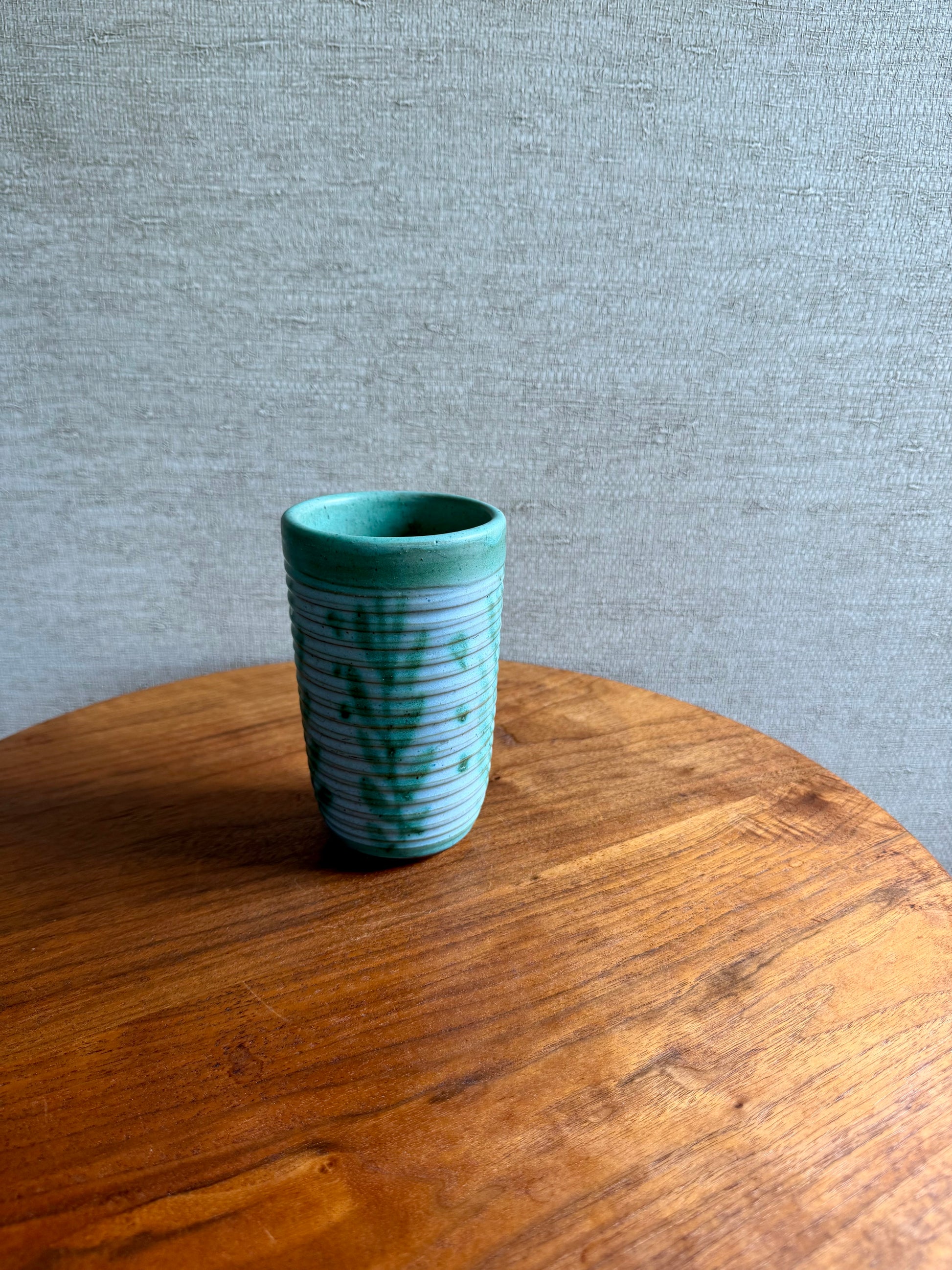 Green ceramic vase with white patterns on a wooden surface and gray background