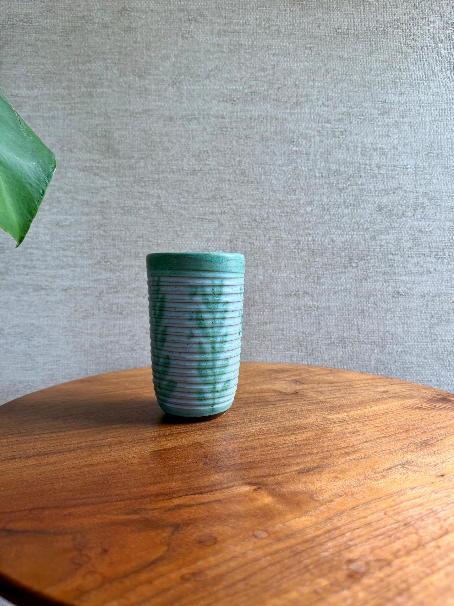 Green ceramic cup on a wooden table with a gray textured wall background
