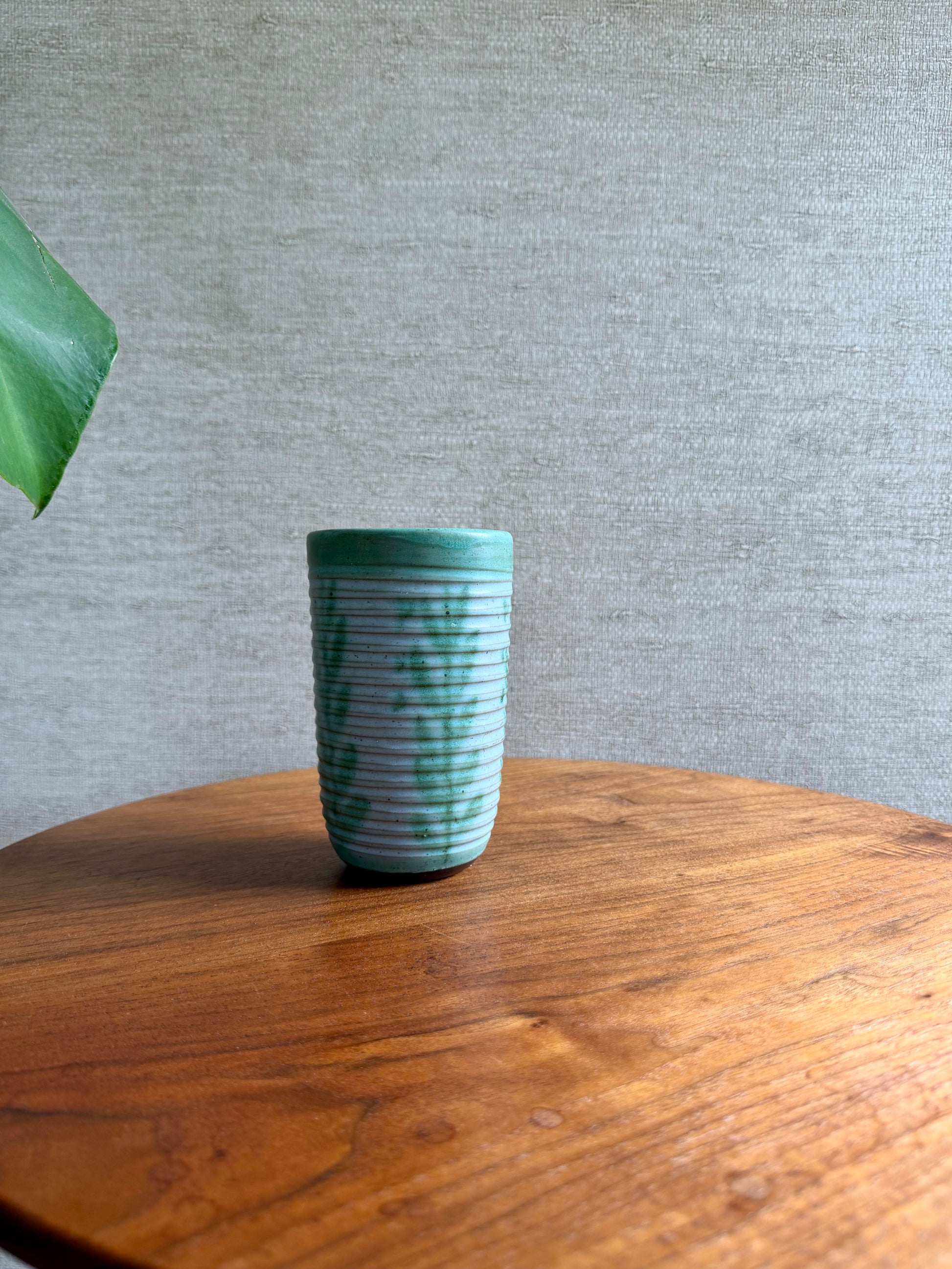 Green ceramic cup on a wooden table with a gray textured wall background