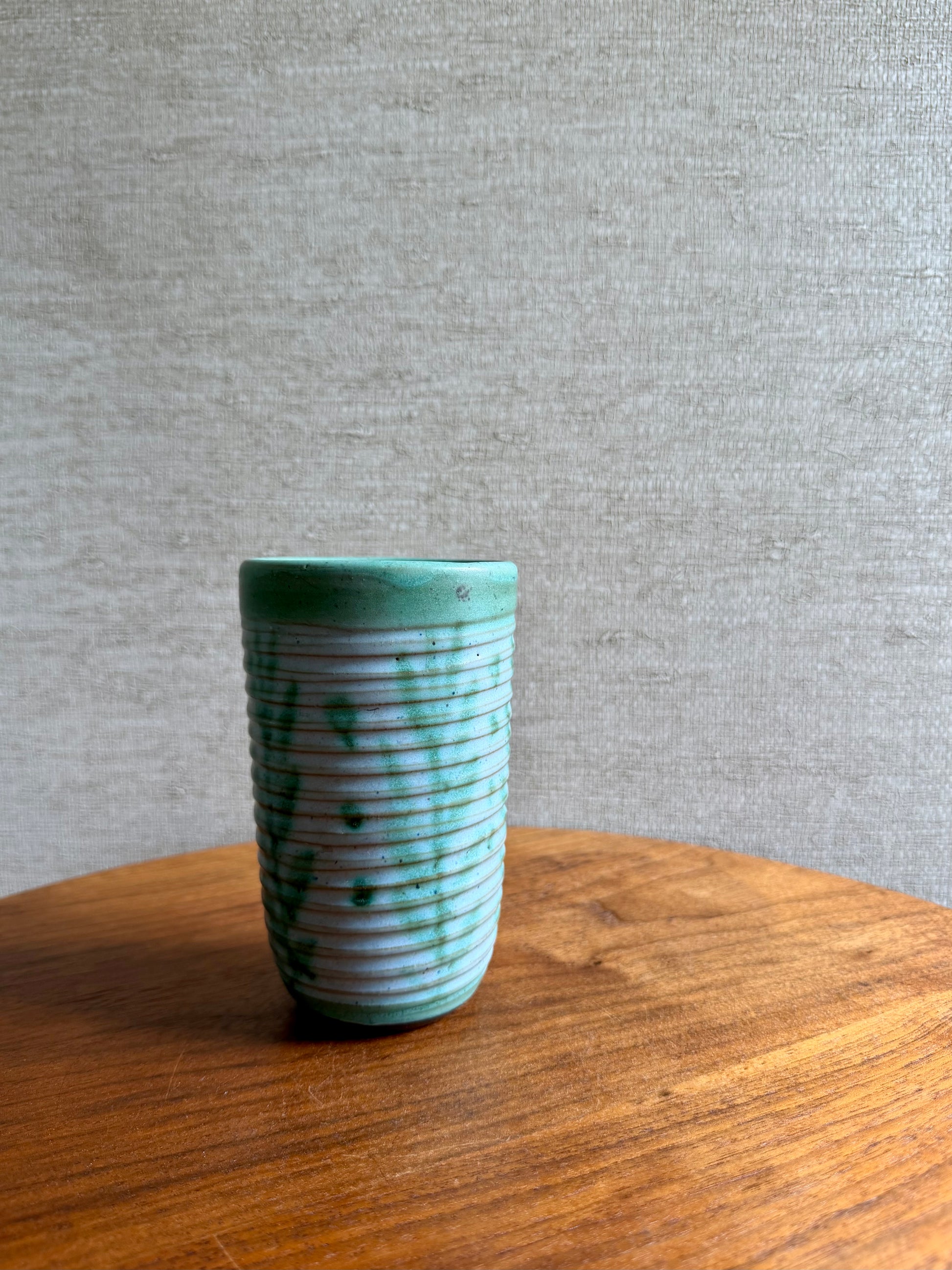 Green ceramic tumbler on a wooden surface with a gray textured background
