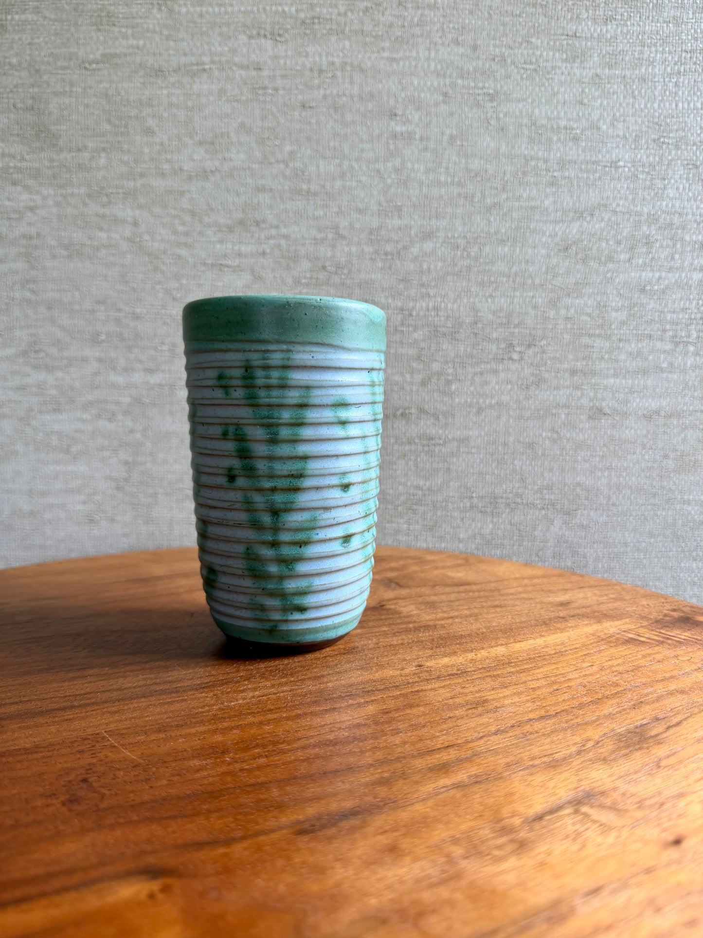Cylindrical ceramic vase with ribbed texture on a wooden surface and gray background
