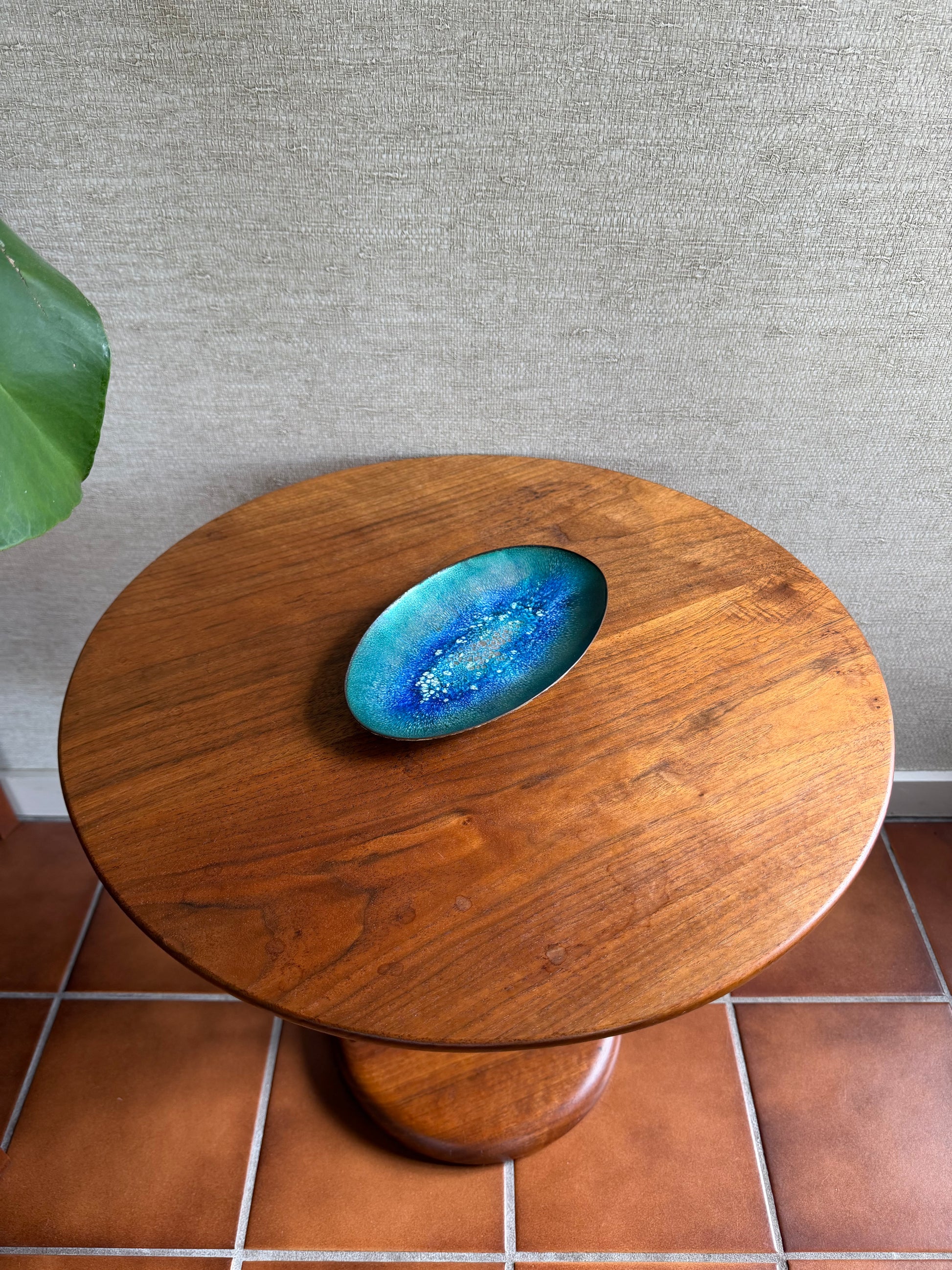 Wooden circular table with a blue glass inset against a tiled wall.