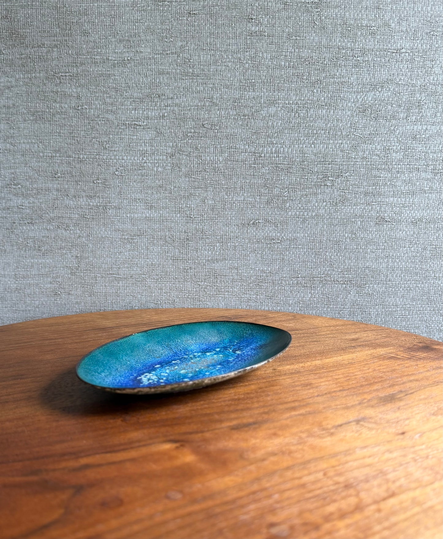 Blue enamel on copper dish on a wooden surface with a gray textured background