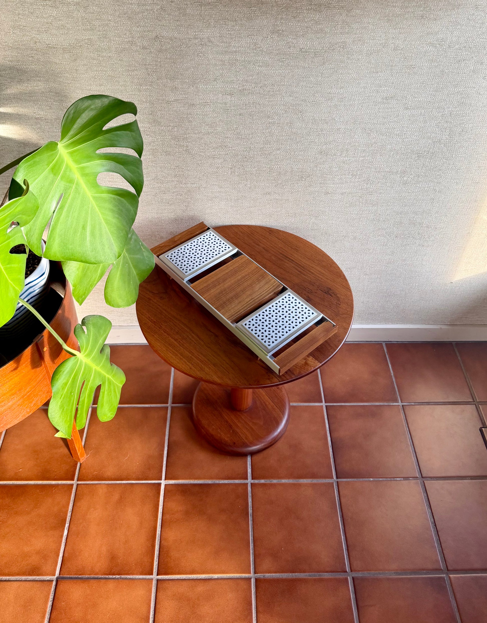 Wooden side table with decorative elements on a tiled floor next to a potted plant.