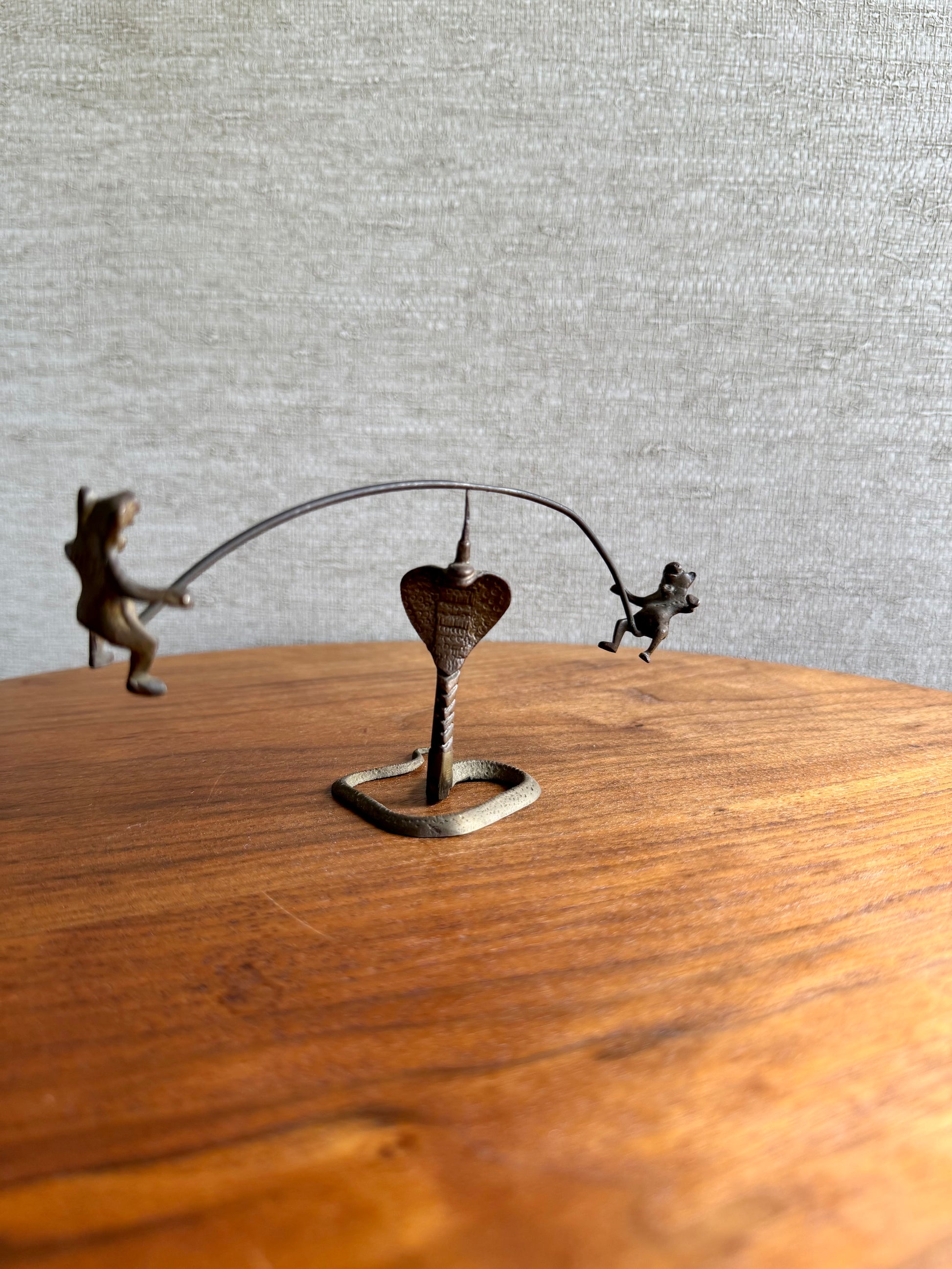 Metal sculpture of two animals playing with a heart on a wooden surface.