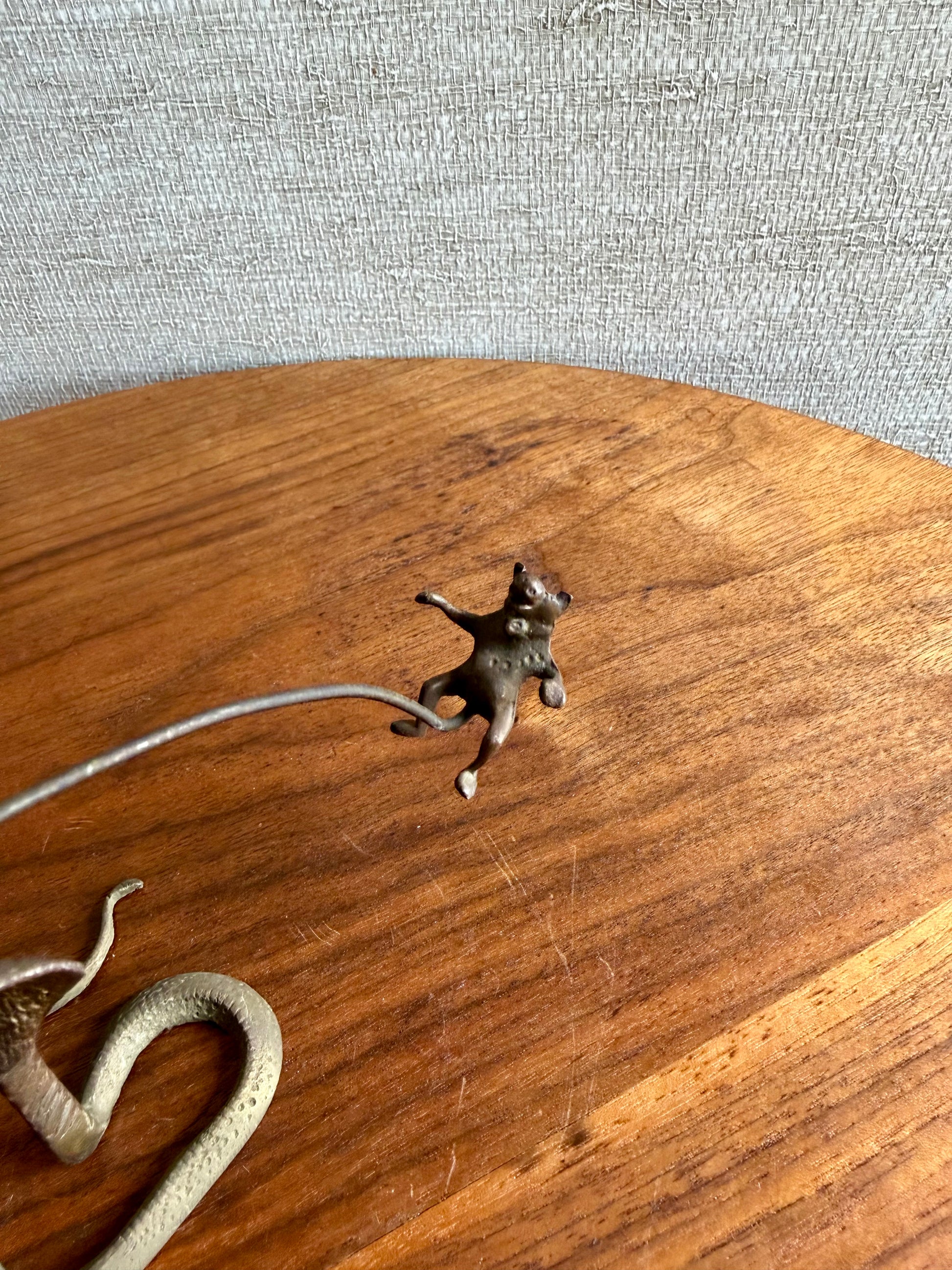 Small bronze figurine of a cat on a wooden surface with a snake nearby.