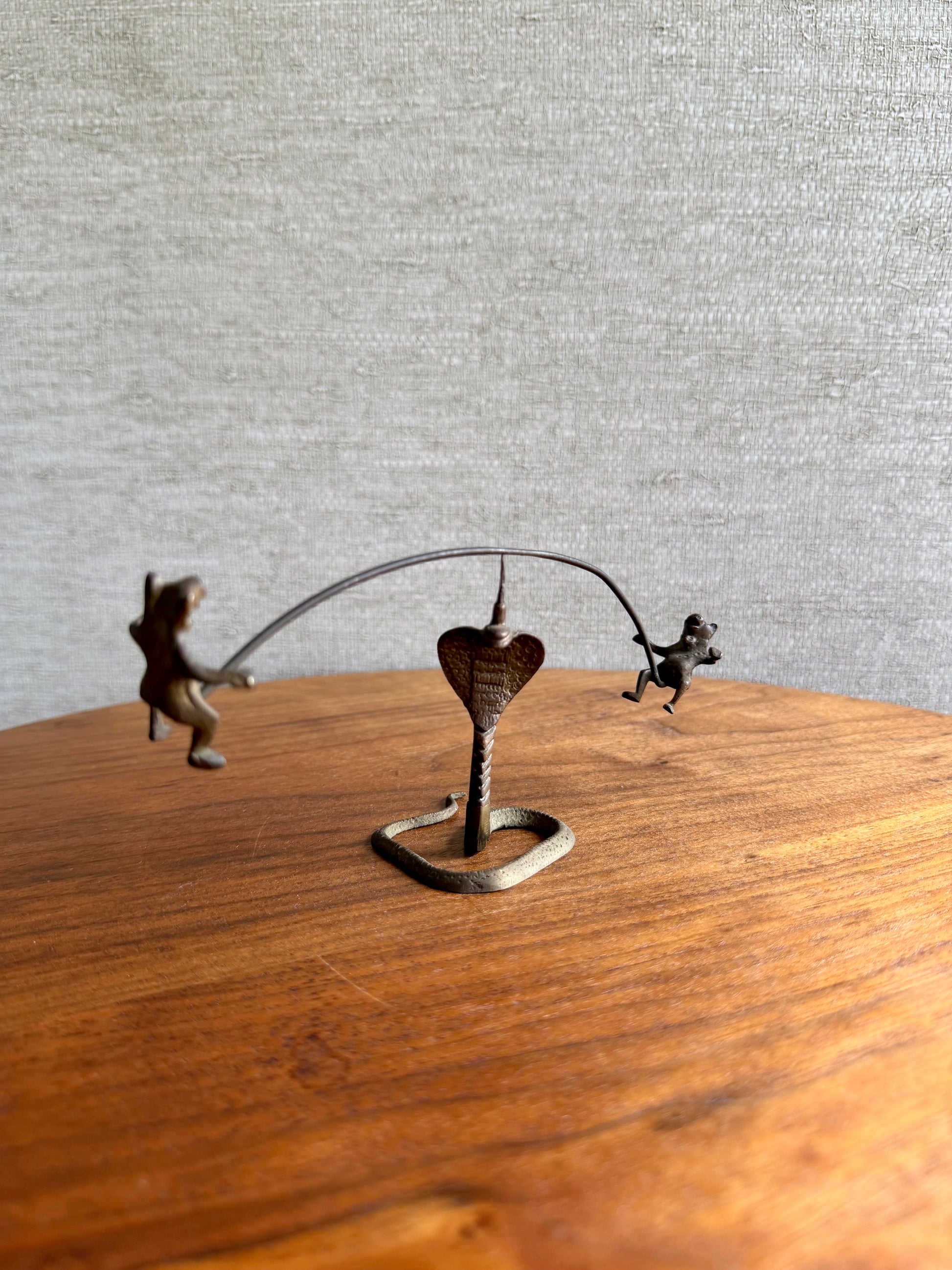 Metallic sculpture of two monkeys on a heart-shaped stand on a wooden surface with a gray textured wall background.
