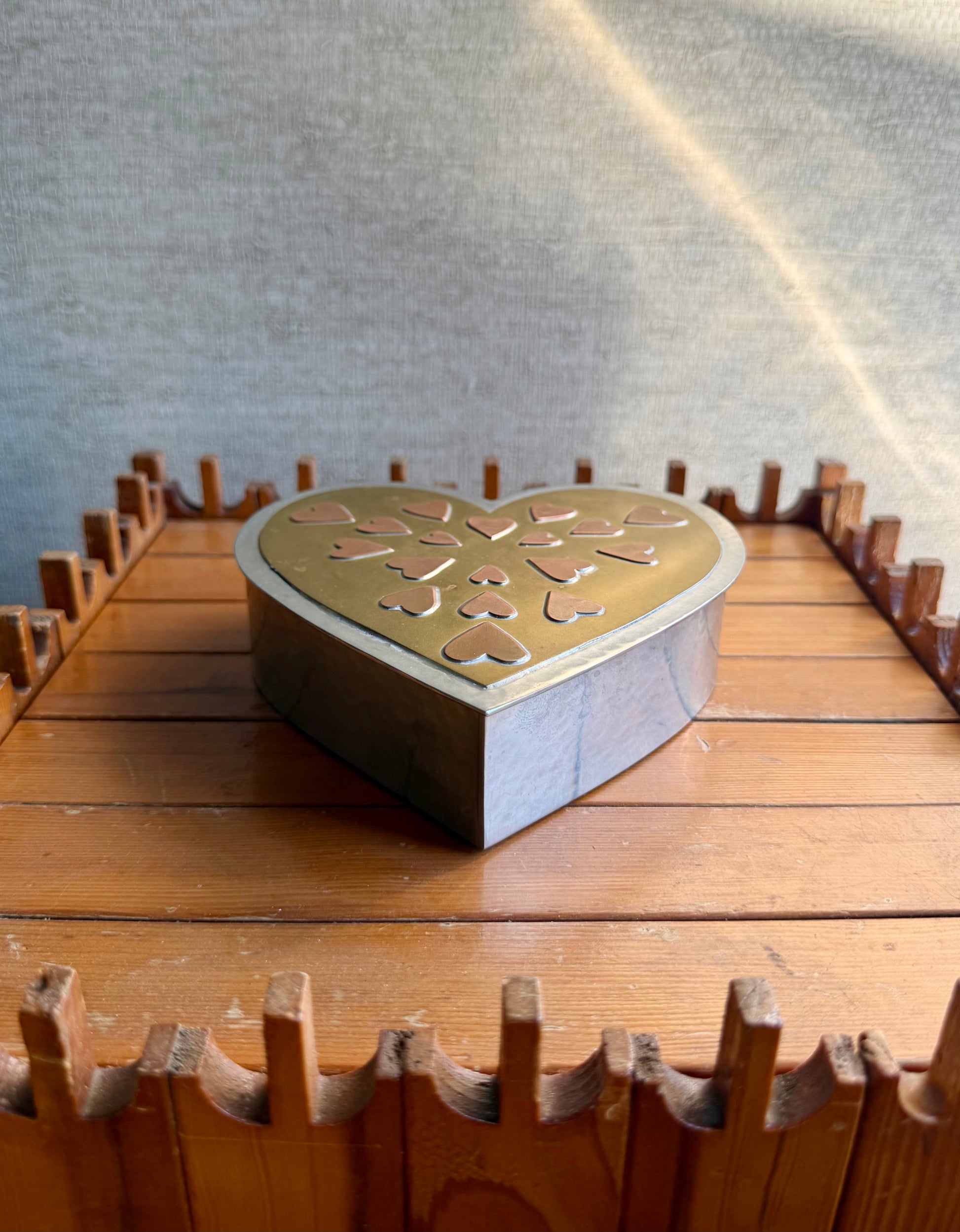 Heart-shaped metal box on a wooden surface with a gray background