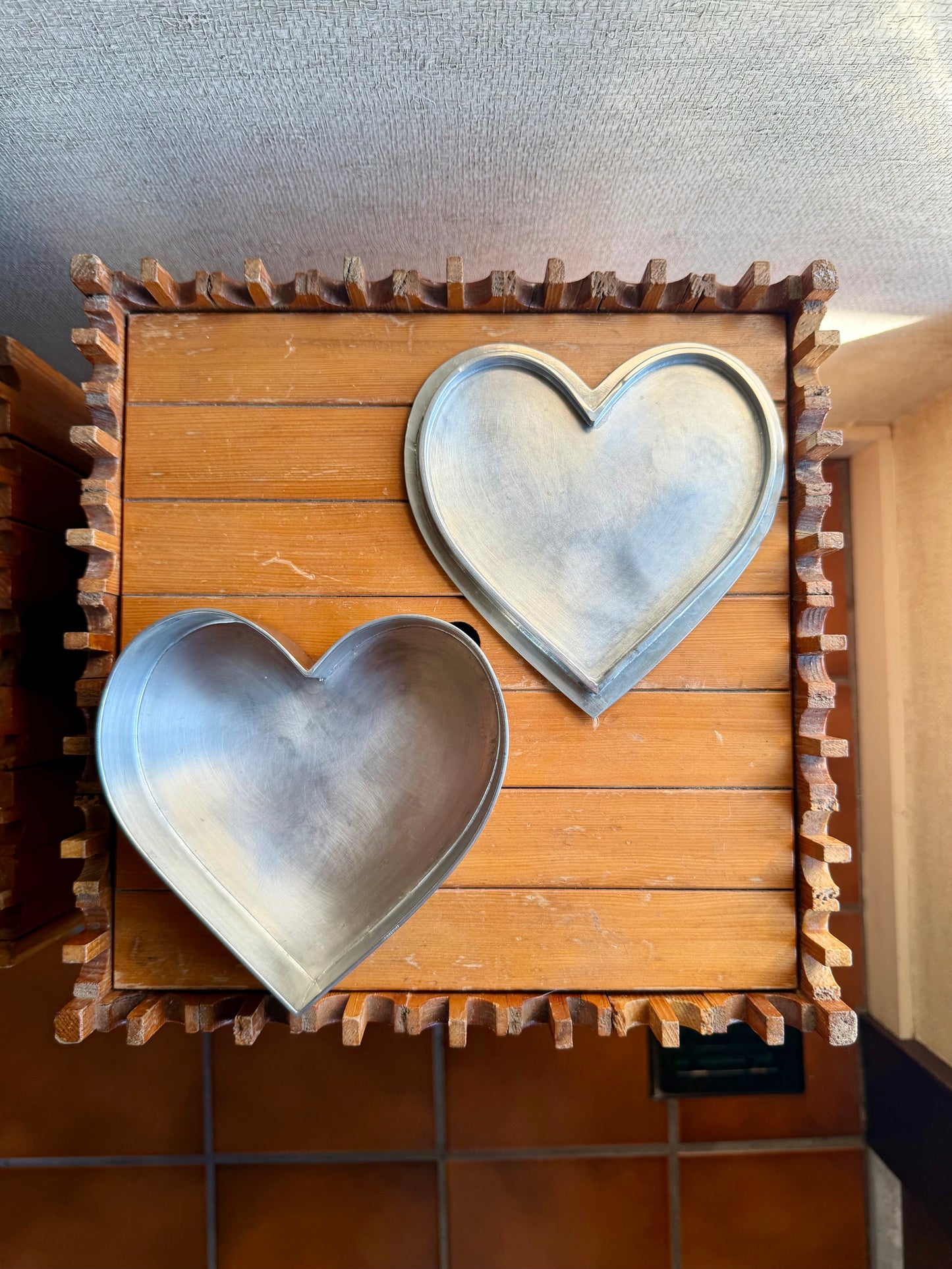 Two metal heart-shaped objects on a wooden crate with a textured wall background.