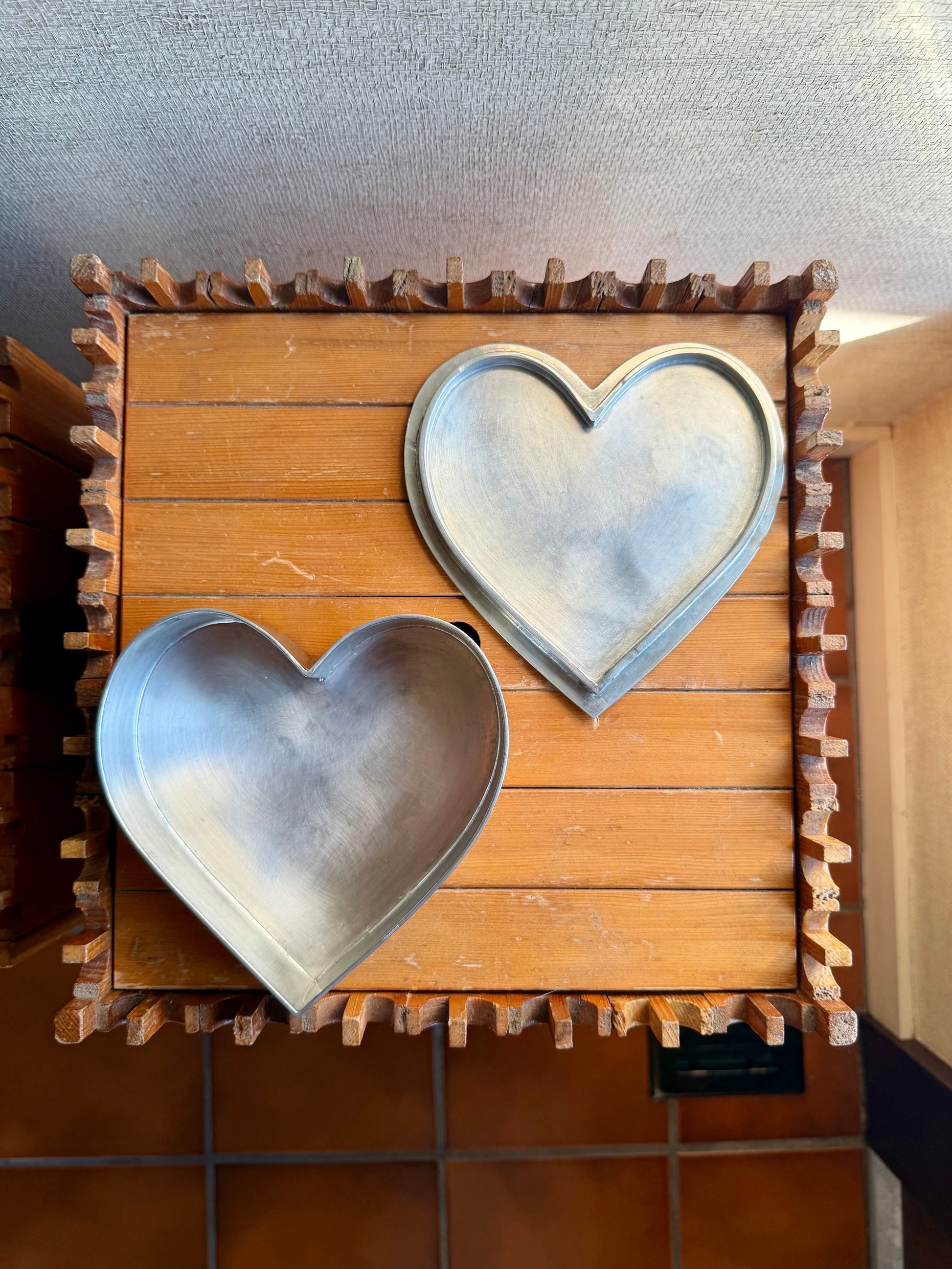 Two metal heart-shaped objects on a wooden crate with a textured wall background.