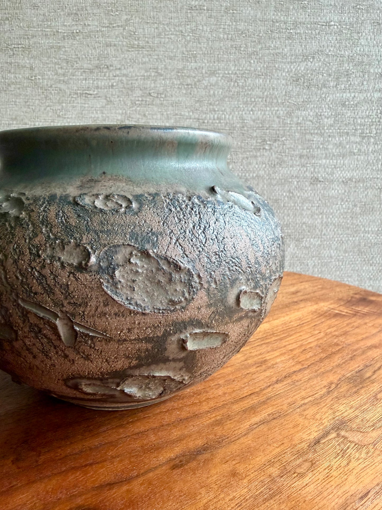 Textured ceramic jar on a wooden surface with a gray textured wall background