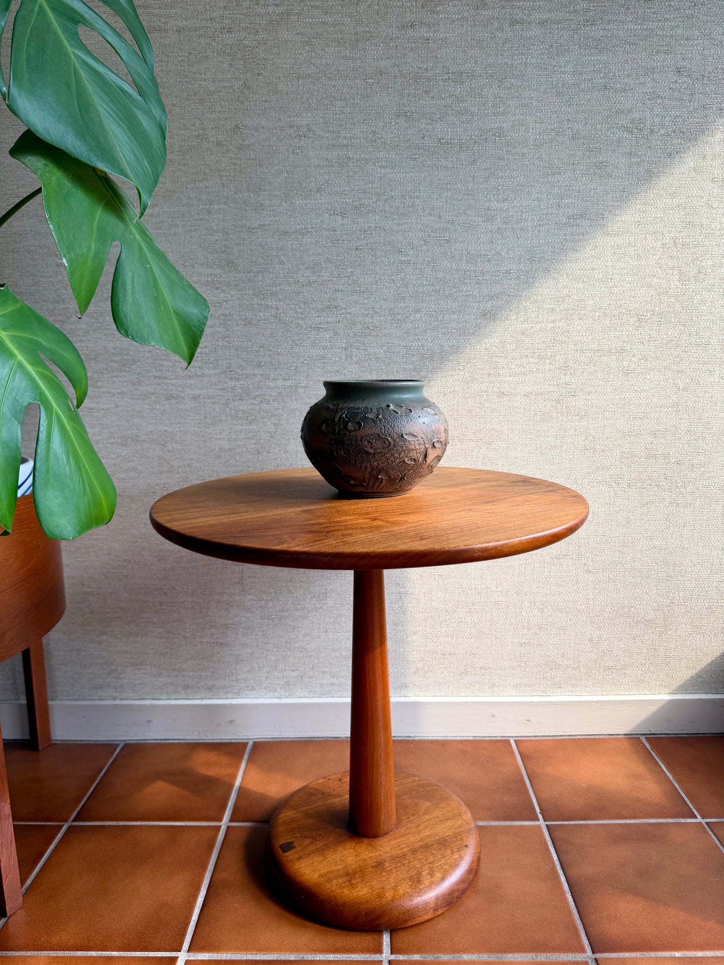 Wooden side table with a vase on a tiled floor against a textured wall.
