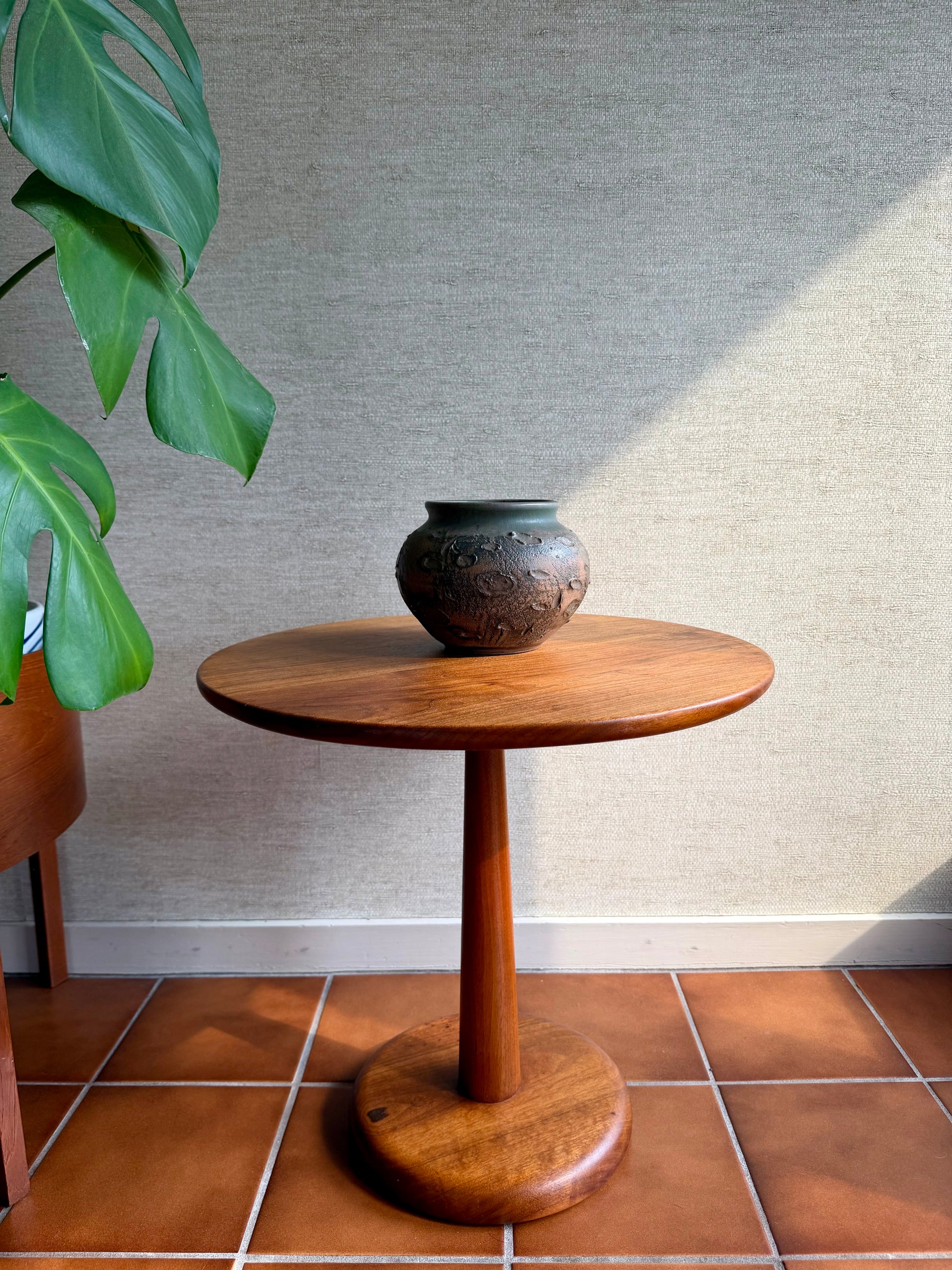 Wooden side table with a vase on a tiled floor against a textured wall.