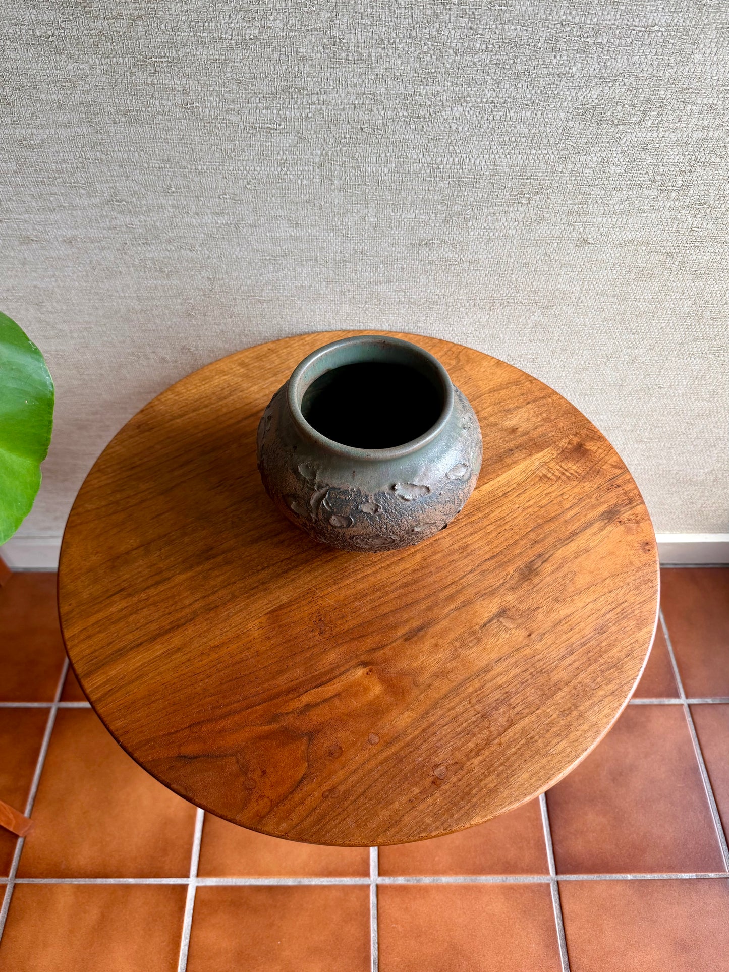Wooden side table with a ceramic vase on a tiled floor against a textured wall.