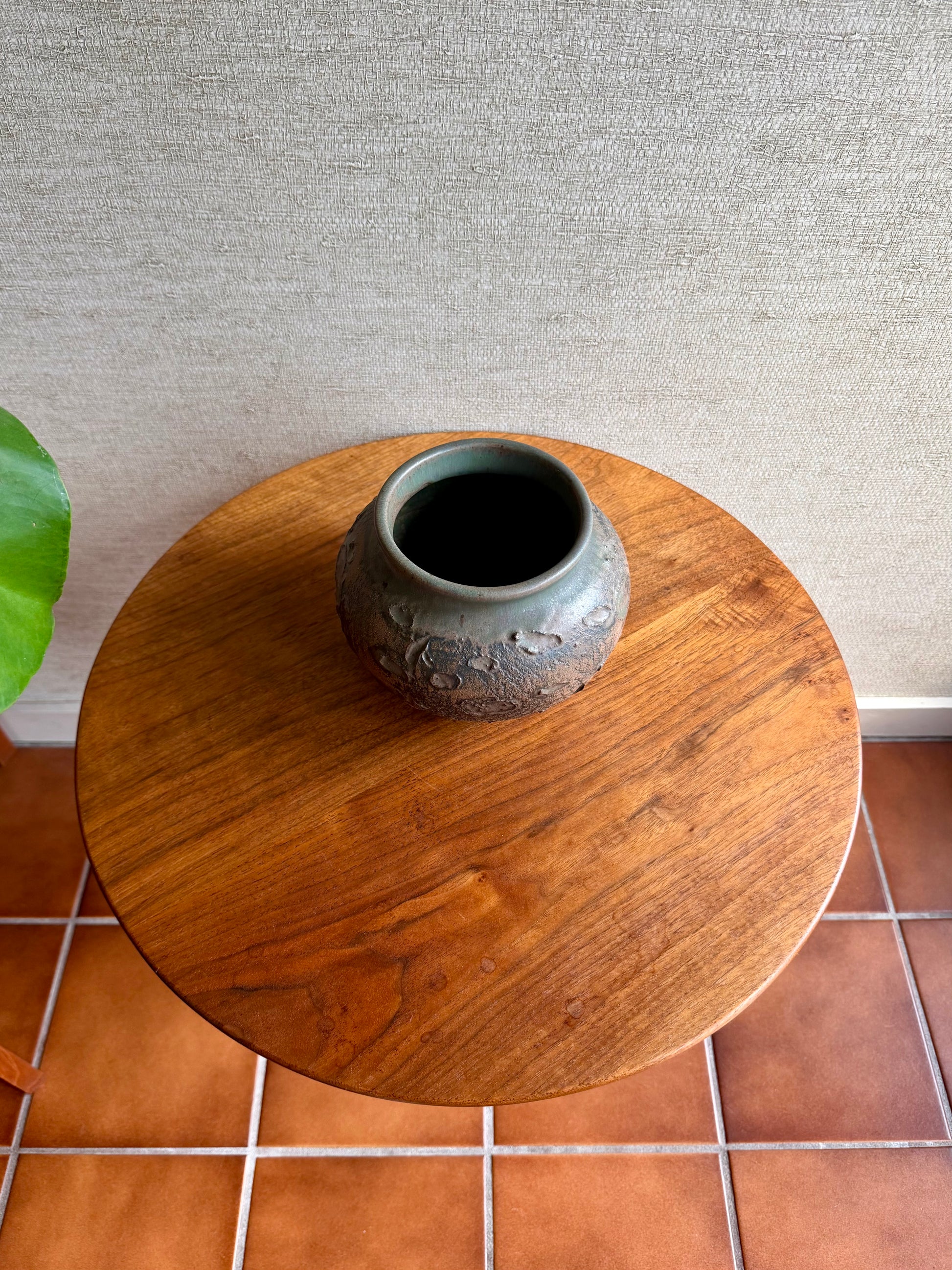 Wooden side table with a ceramic vase on a tiled floor against a textured wall.