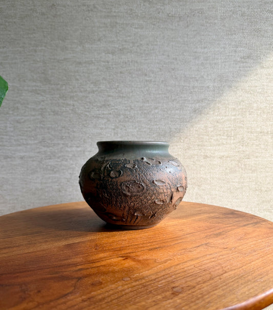 Textured ceramic vase on a wooden surface with a neutral background