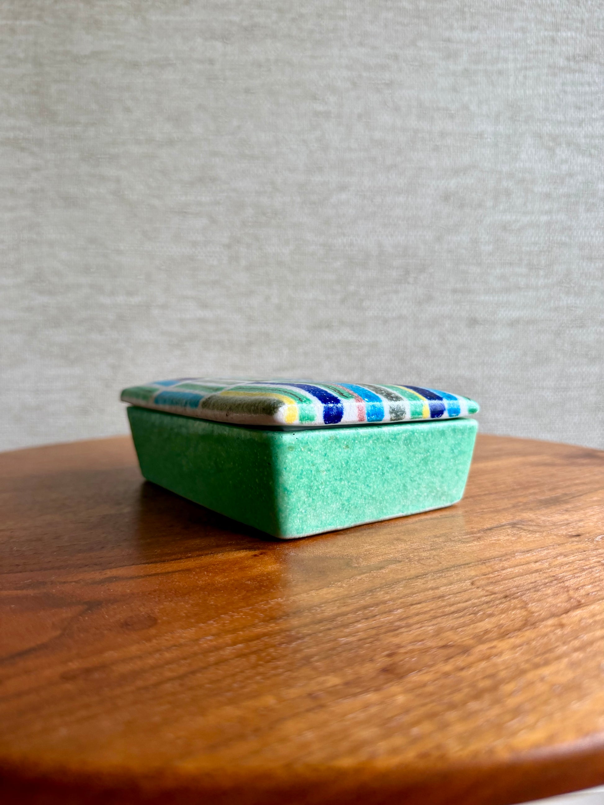 Green rectangular box with a colorful striped lid on a wooden surface.