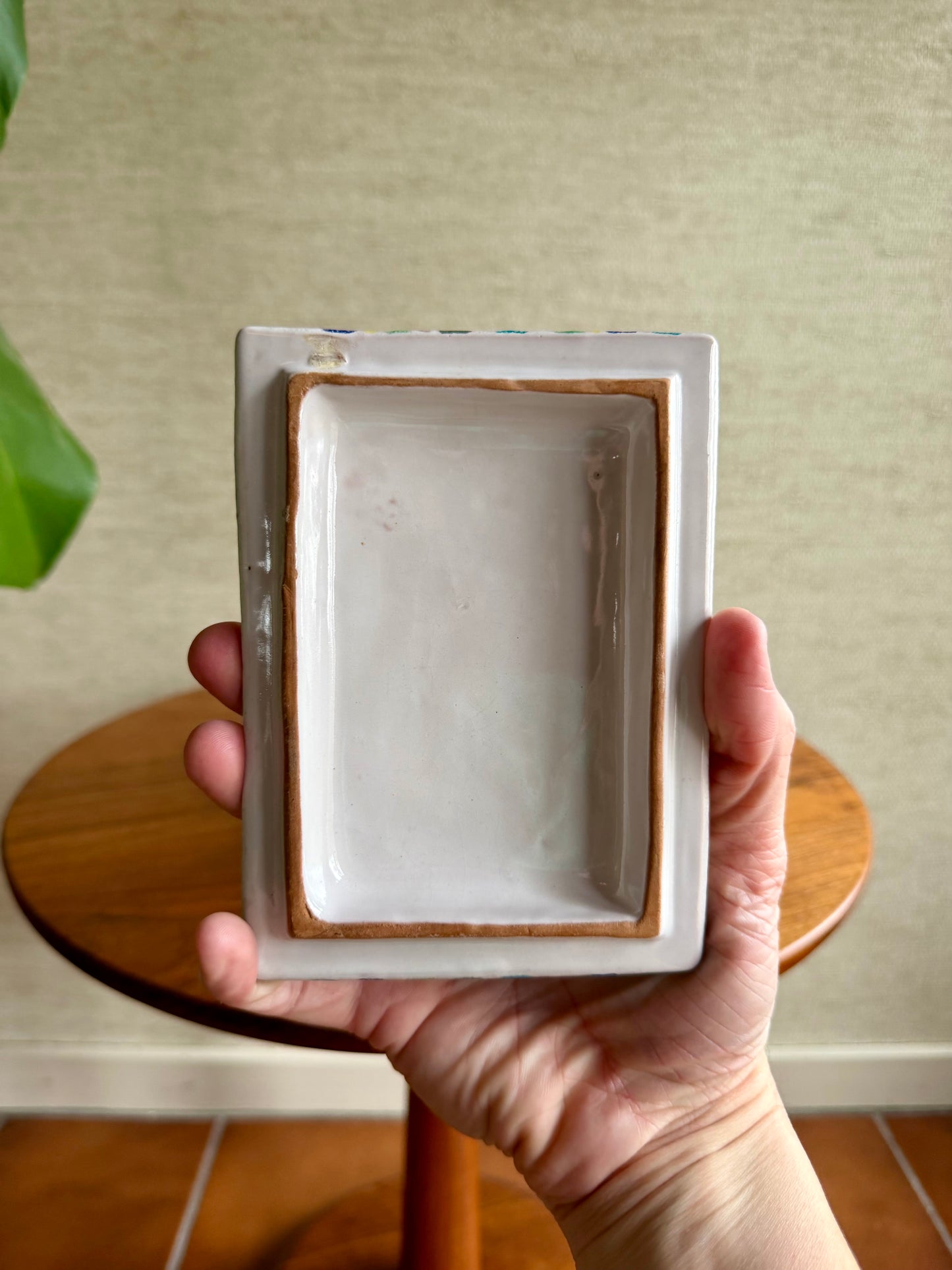 Hand holding a small rectangular ceramic dish with a plain background