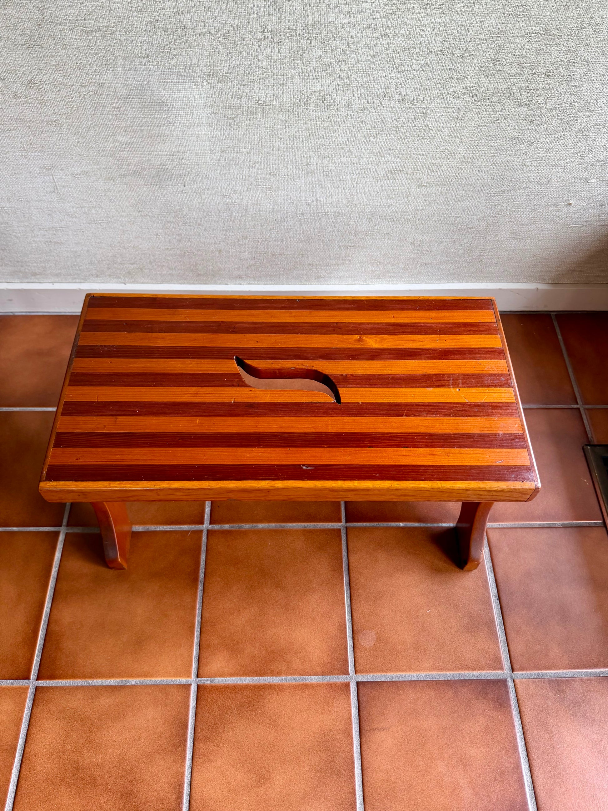 Wooden step stool on a tiled floor against a textured wall.