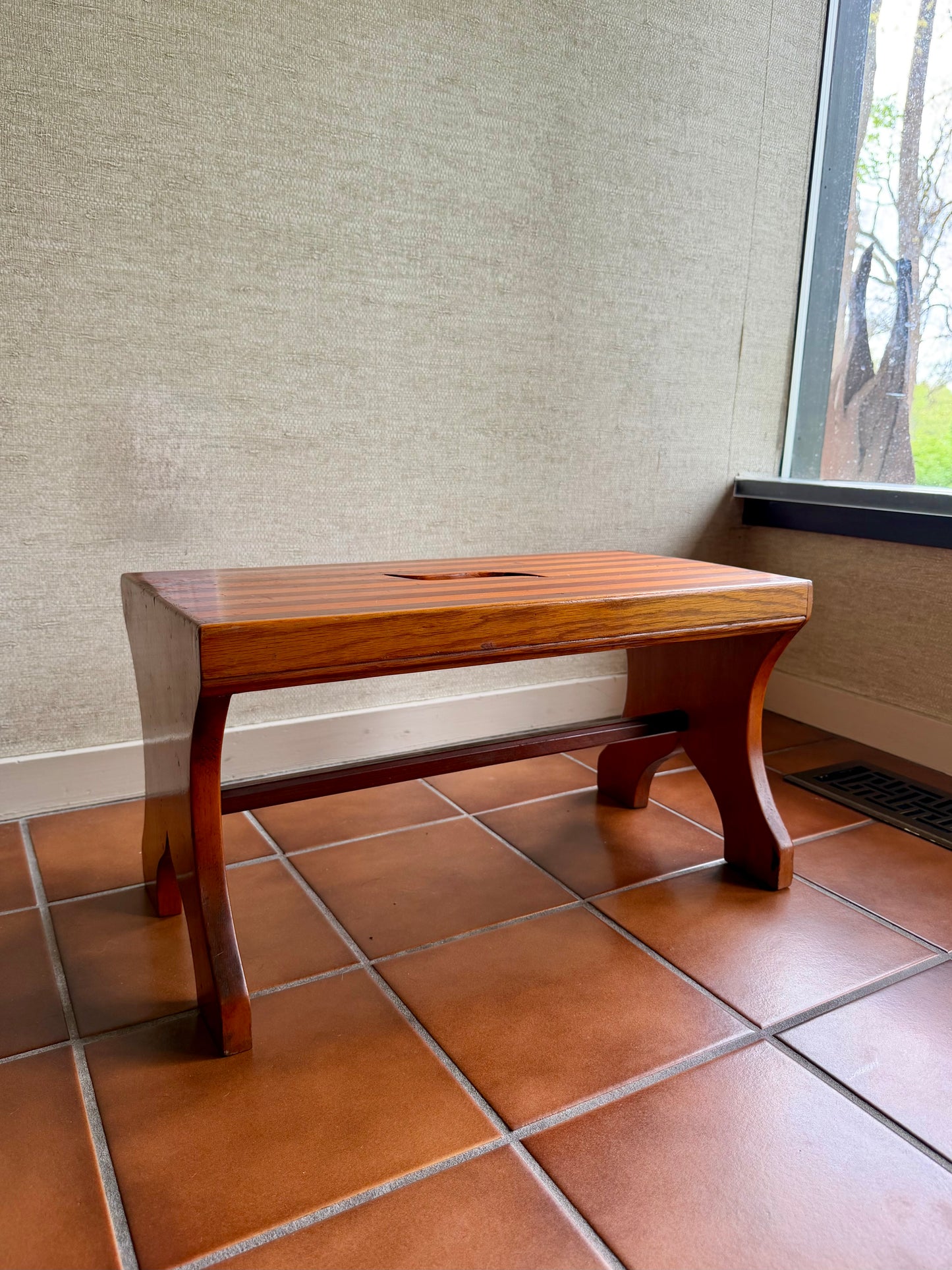 Wooden step stool on a tiled floor against a textured wall.