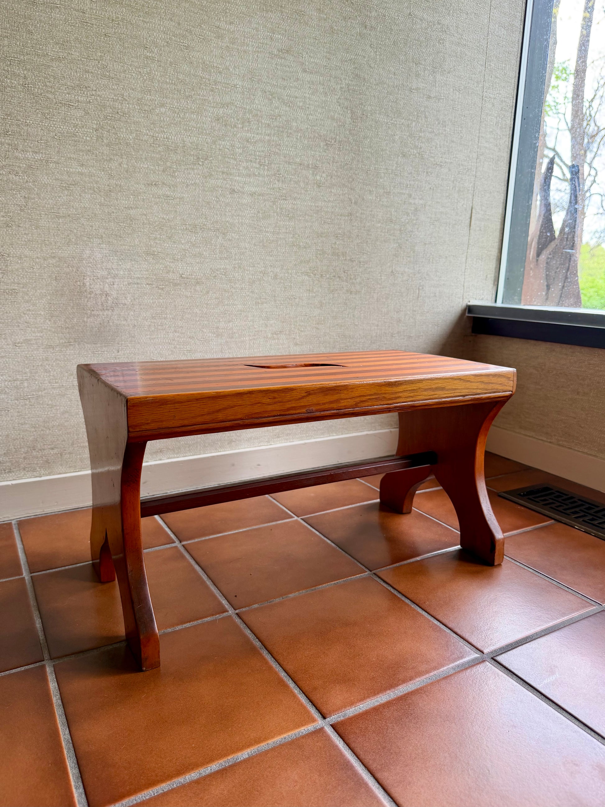 Wooden step stool on a tiled floor against a textured wall.