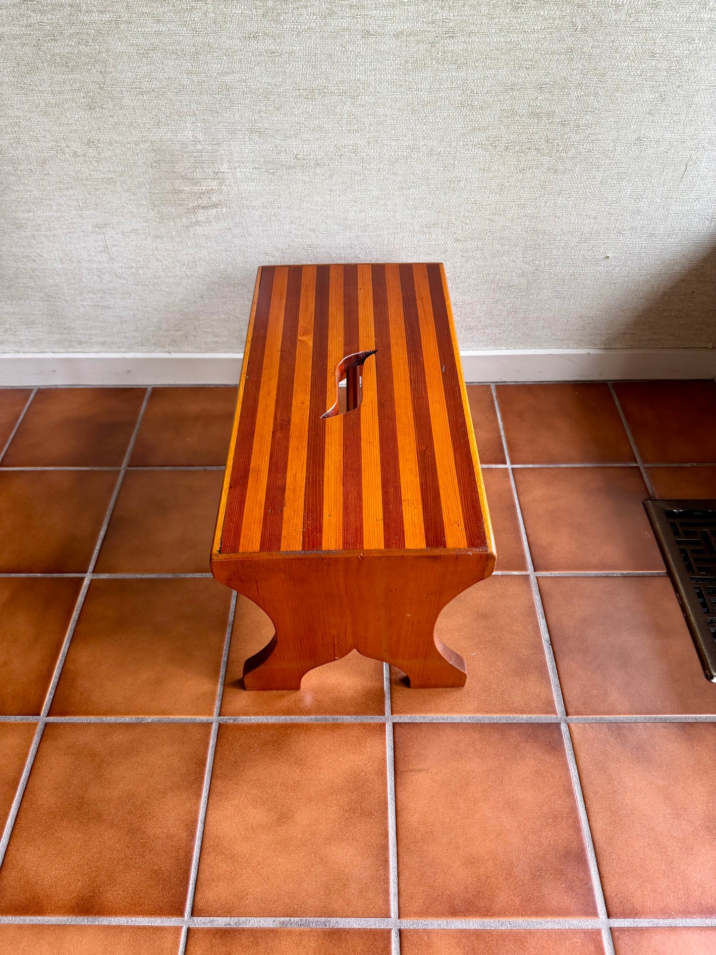 Wooden step stool on a tiled floor with a textured wall background