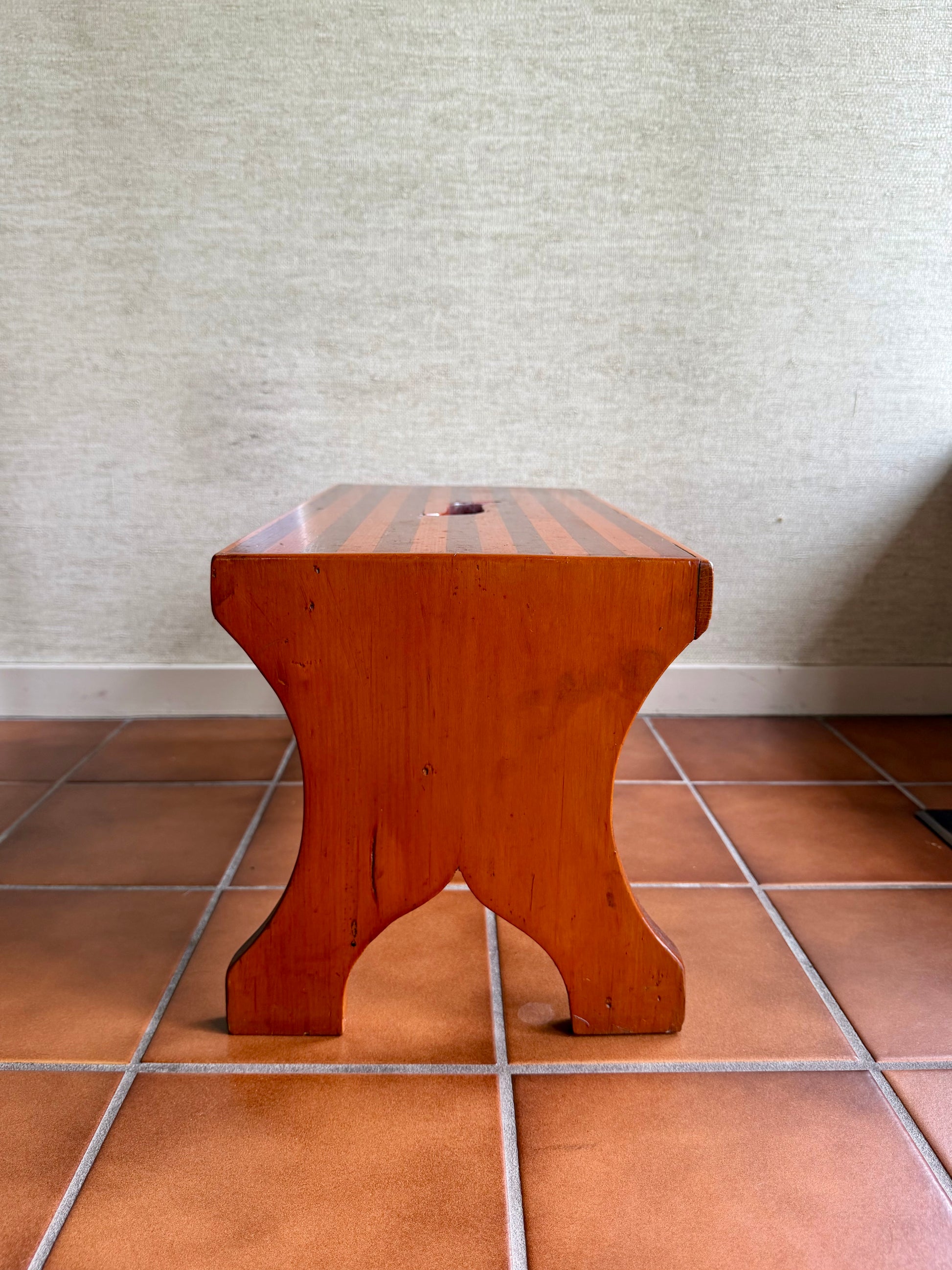 Wooden stool on a tiled floor with a textured wall background