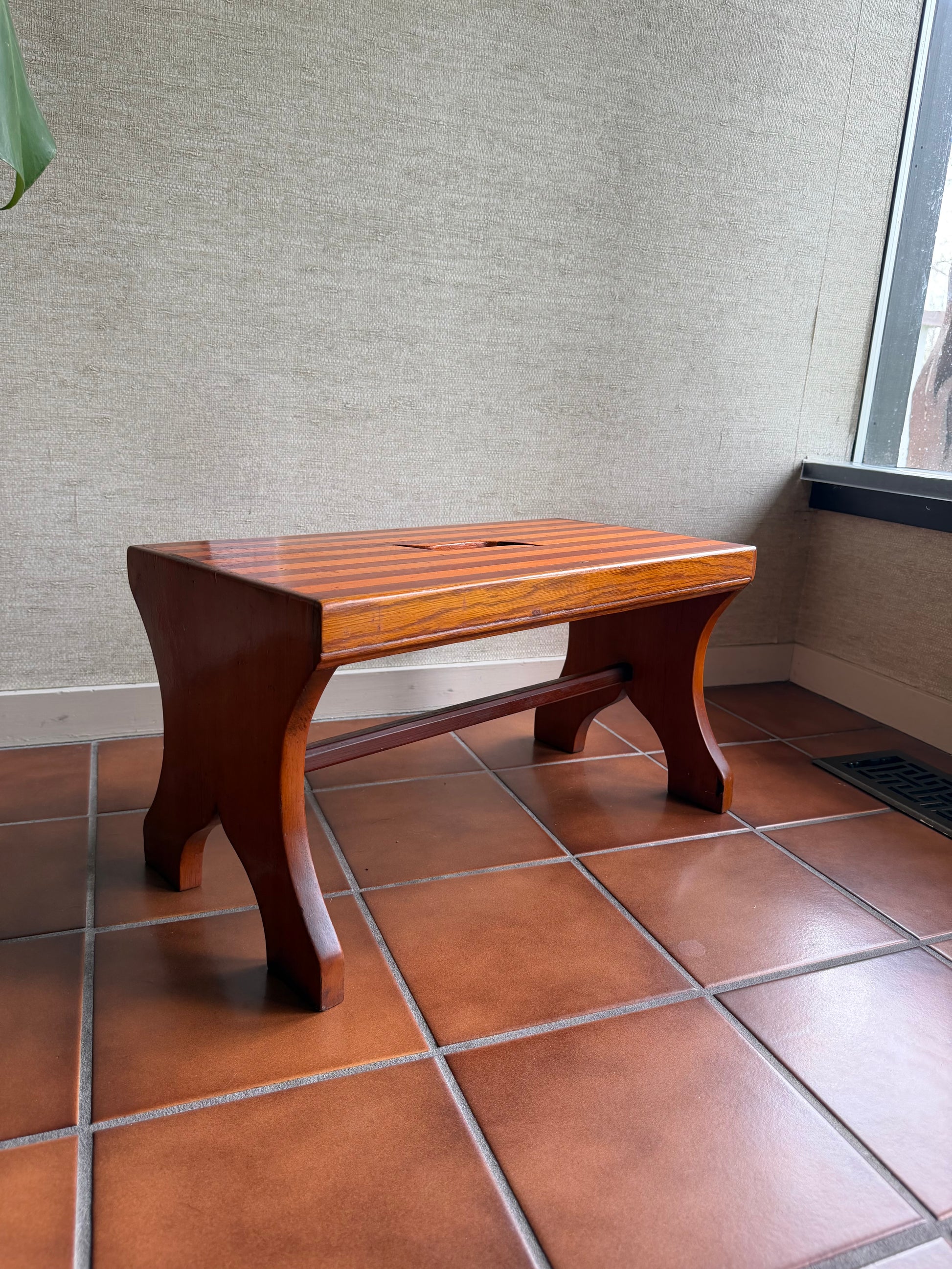 Wooden stool on a tiled floor with a textured wall in the background