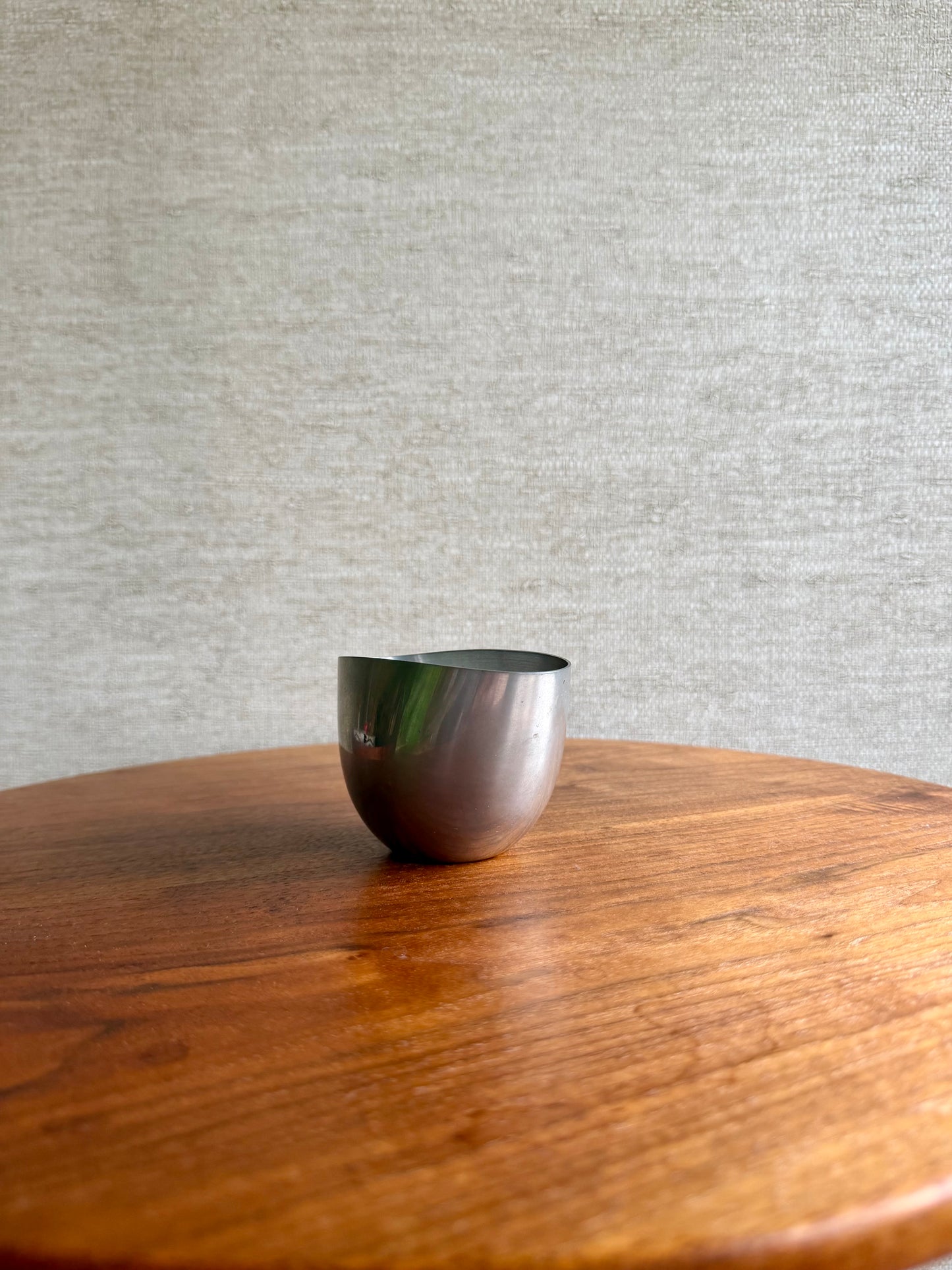 Silver bowl on a wooden surface with a gray textured wall in the background