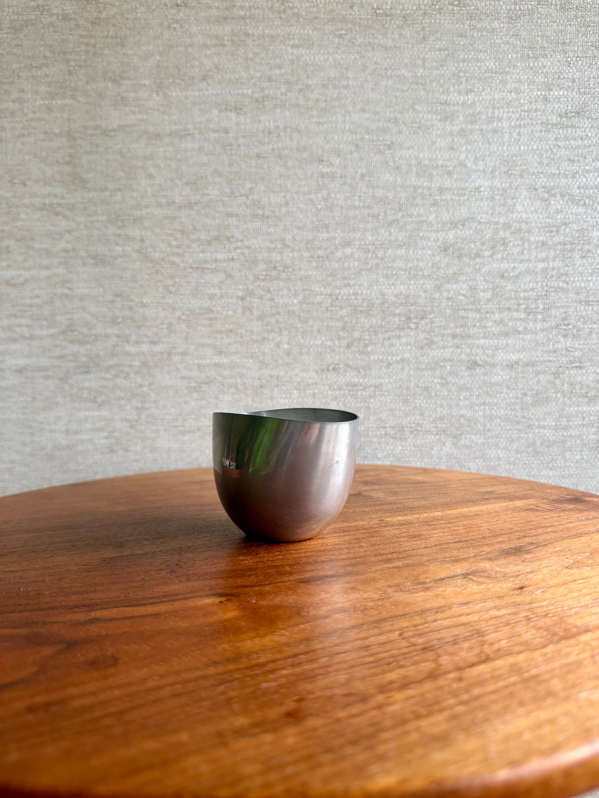 Silver bowl on a wooden surface with a gray textured wall in the background