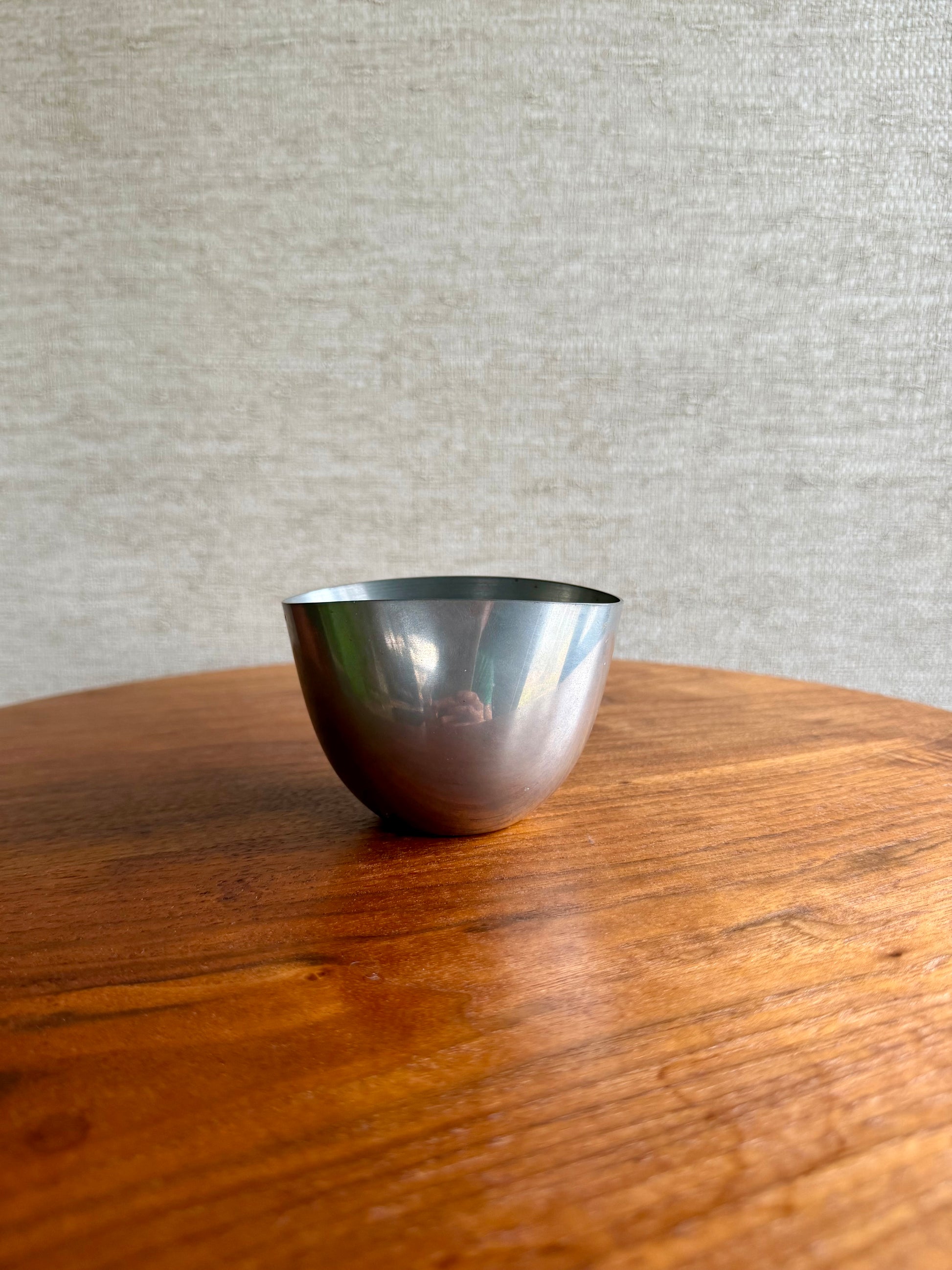 Silver bowl on a wooden surface with a gray textured wall background