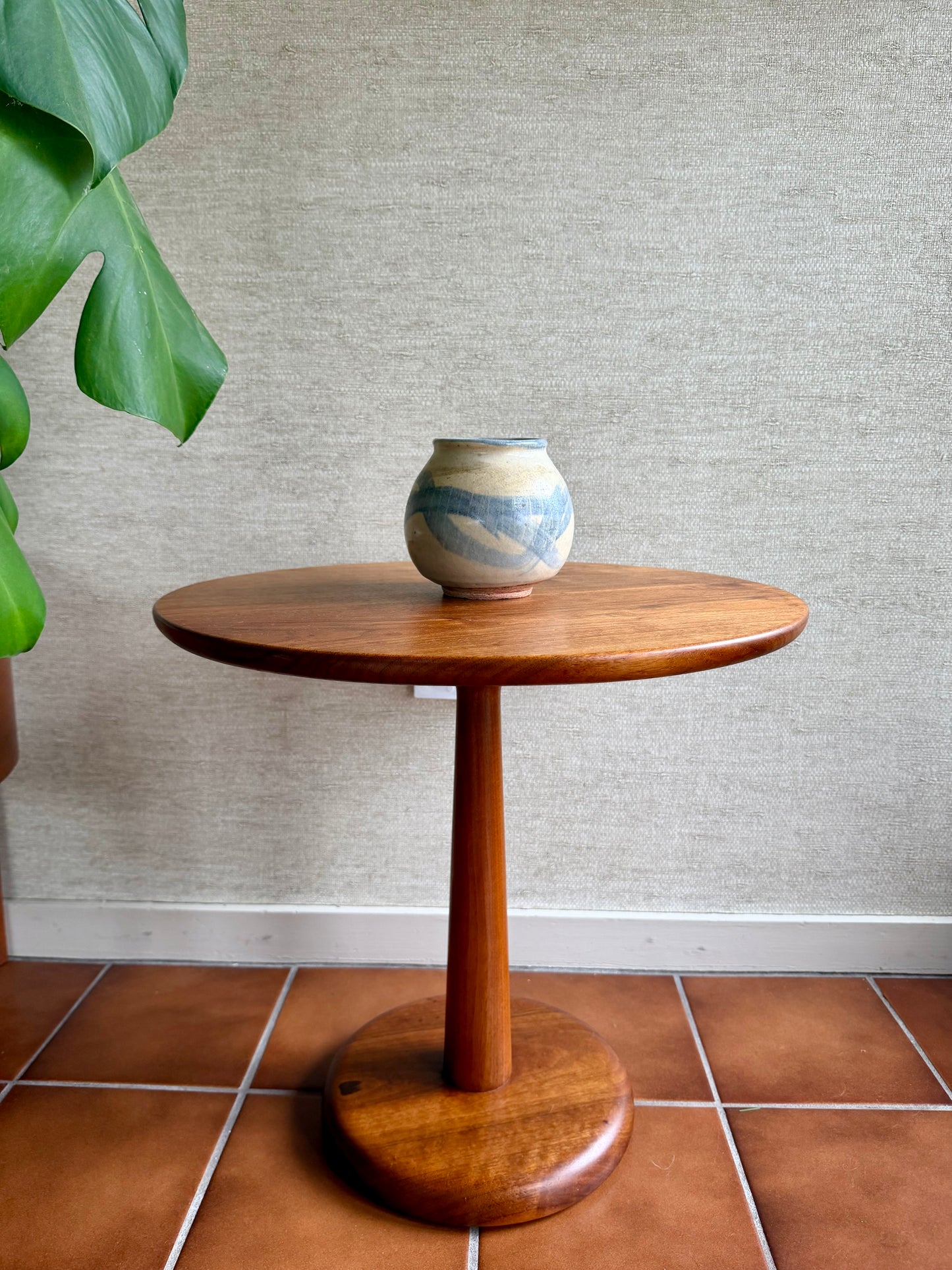 Wooden side table with a ceramic vase on a tiled floor against a textured wall.