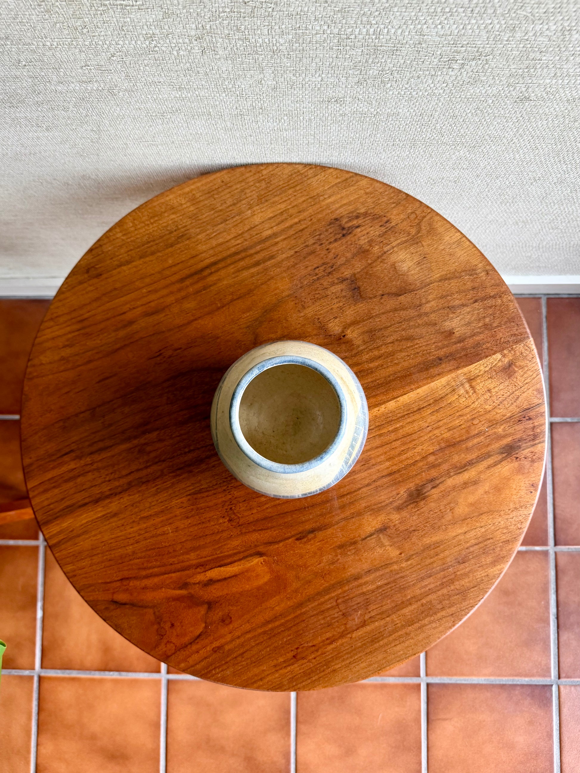 Wooden round table with a white vase on a tiled floor