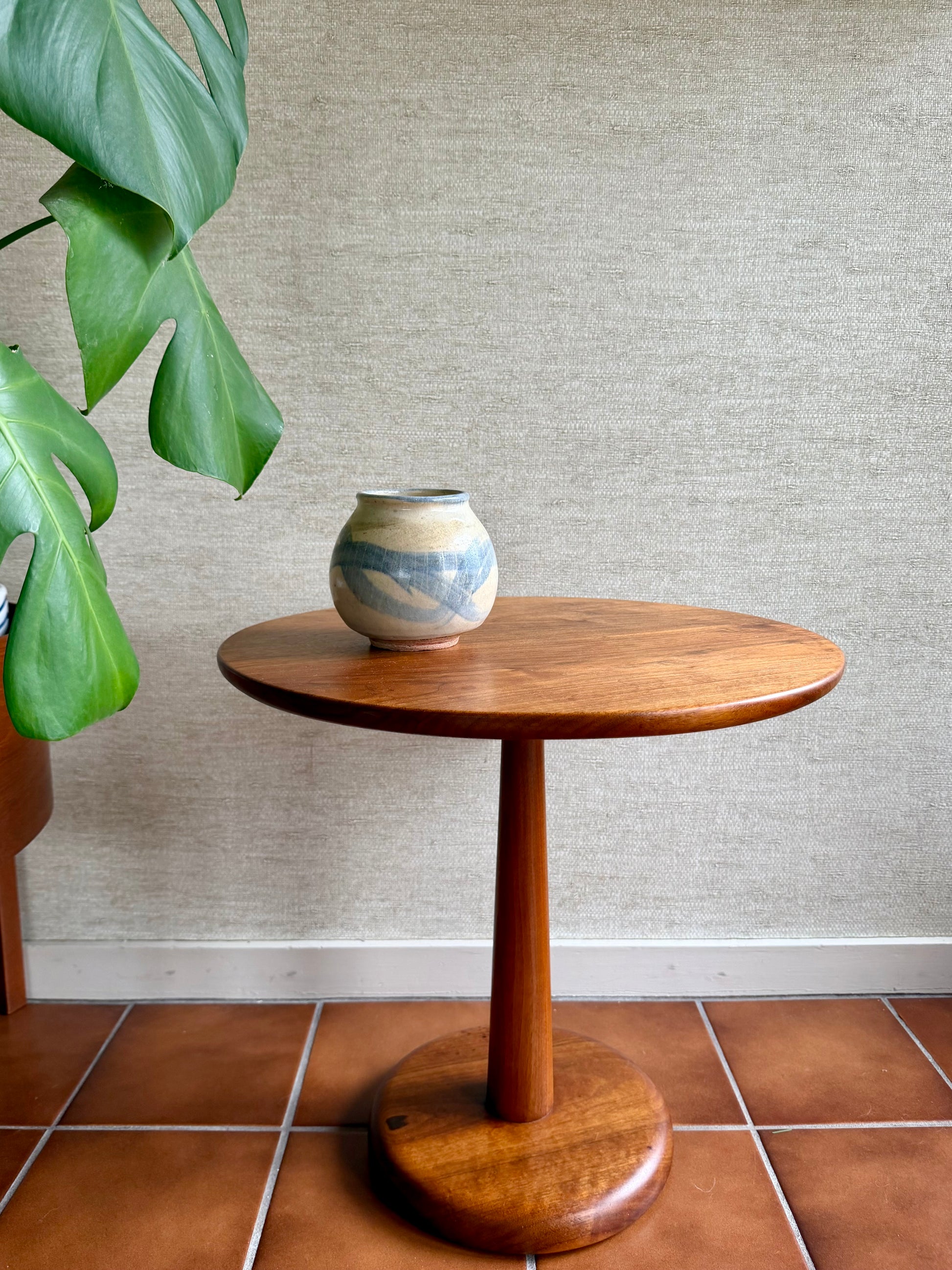 Wooden side table with a ceramic vase against a textured wall.